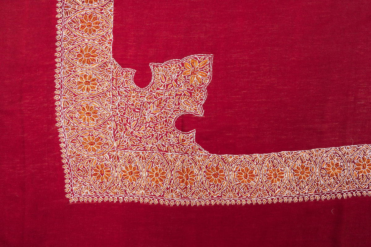 Corner of a crimson rumal with a broad gold-and-ivory floral border and a large embroidered motif extending inward