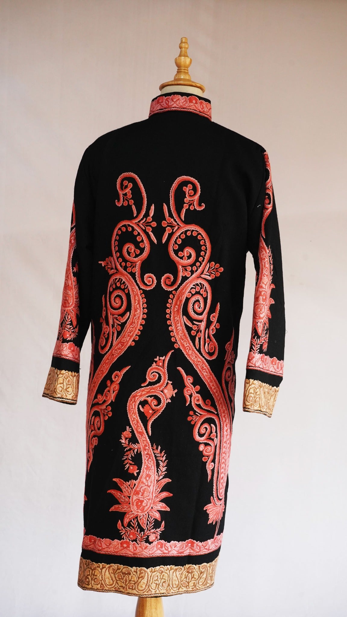 Full back of the black jacket with long symmetrical coral-pink paisleys and a golden embroidered hem border