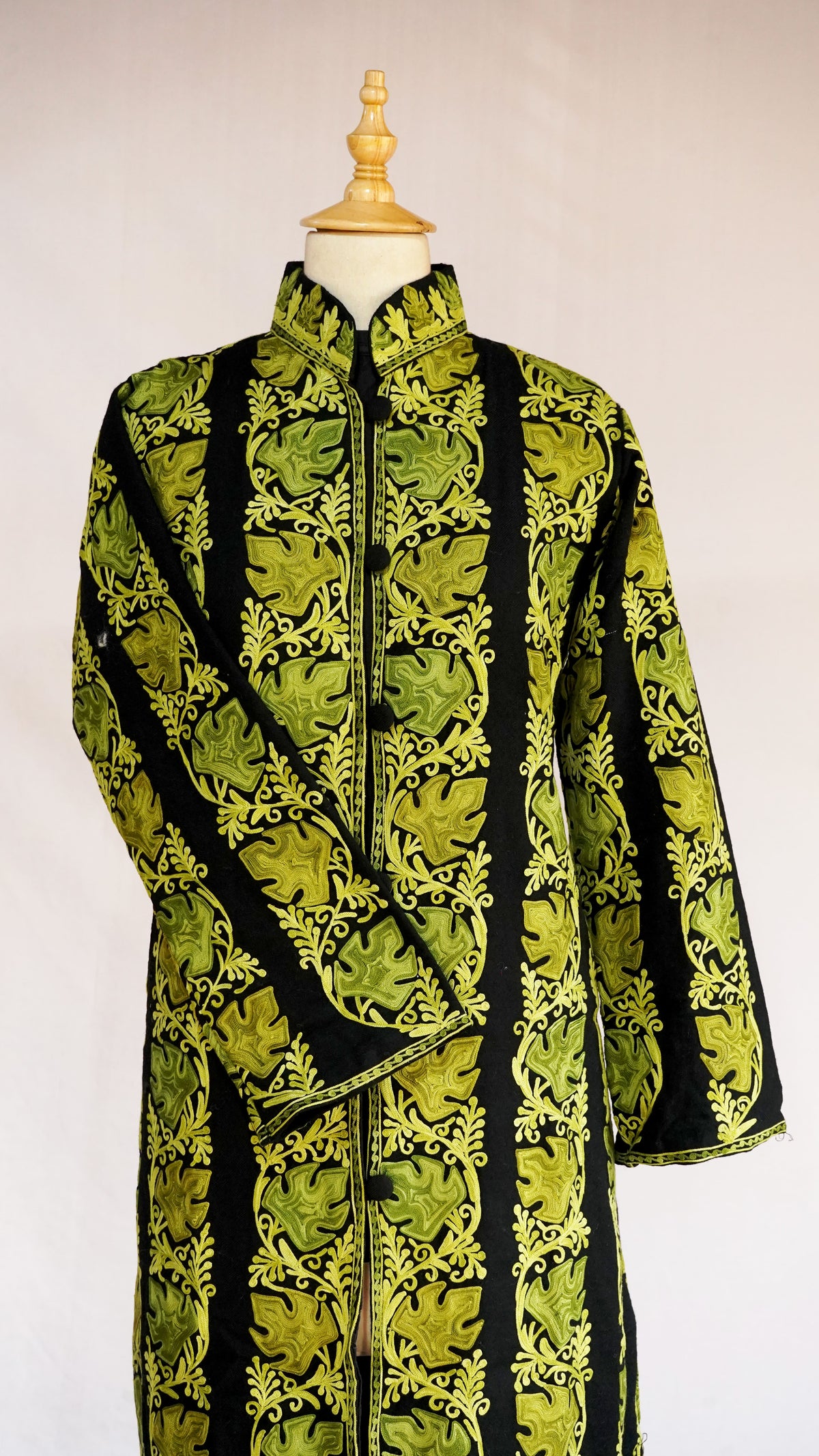 Front view of the black jacket with one sleeve across the body and chartreuse embroidered bands from collar to hem.