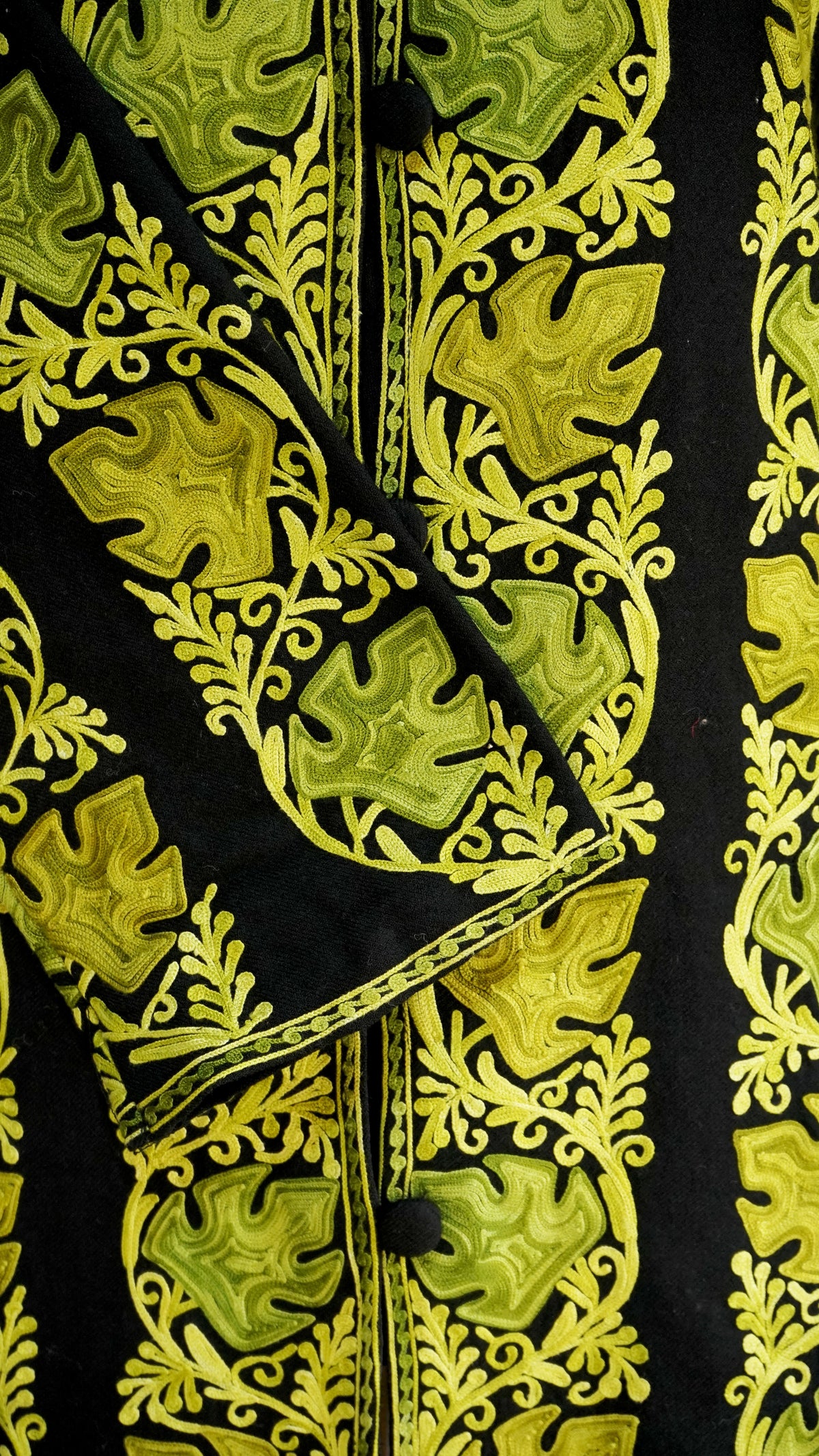 Close-up of the black jacket’s cuff across the buttoned front, with chartreuse leaves and fine curling embroidery.