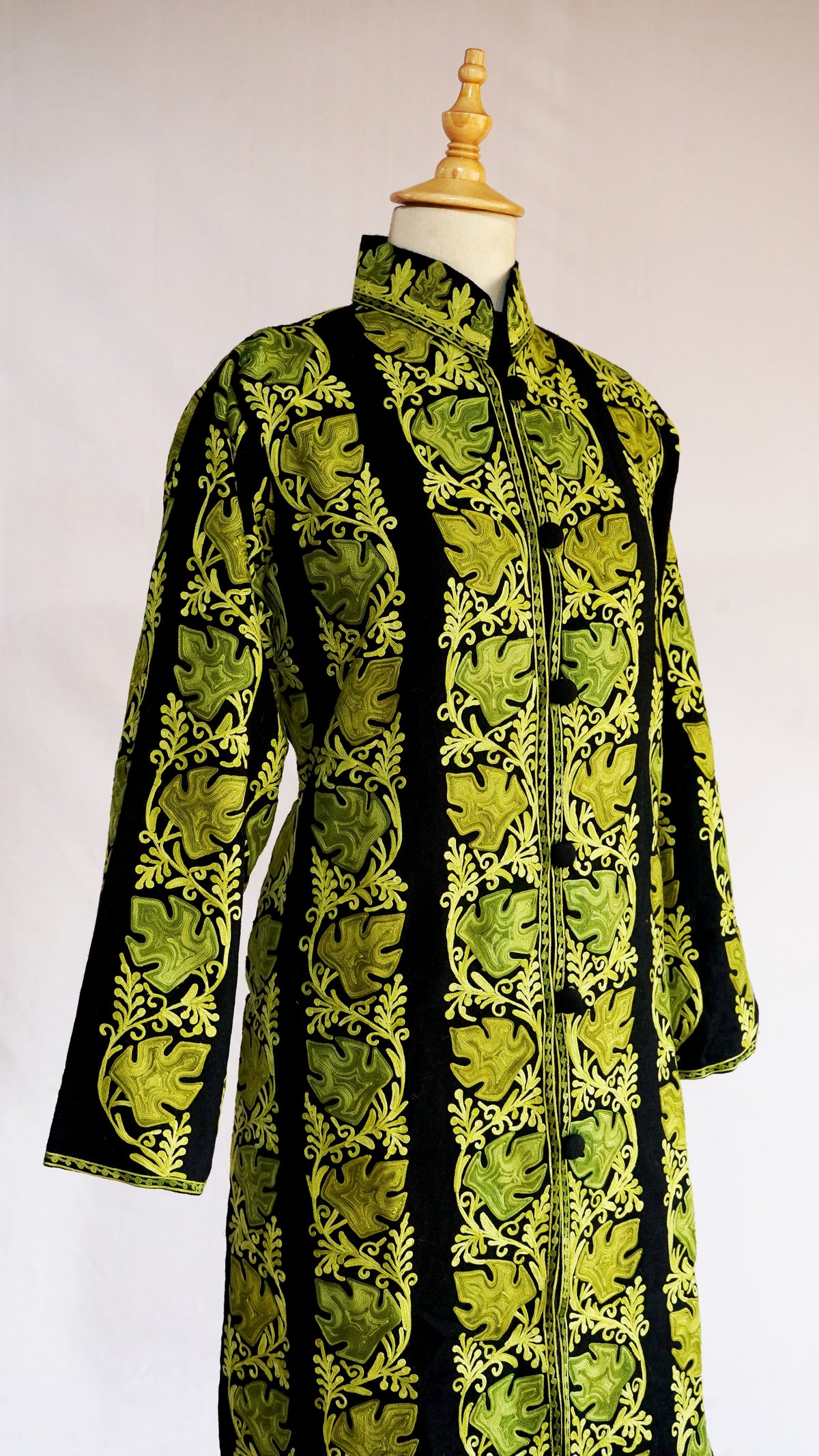 Angled front view of the black jacket with vertical chartreuse leaf-and-vine bands and an embroidered stand collar.