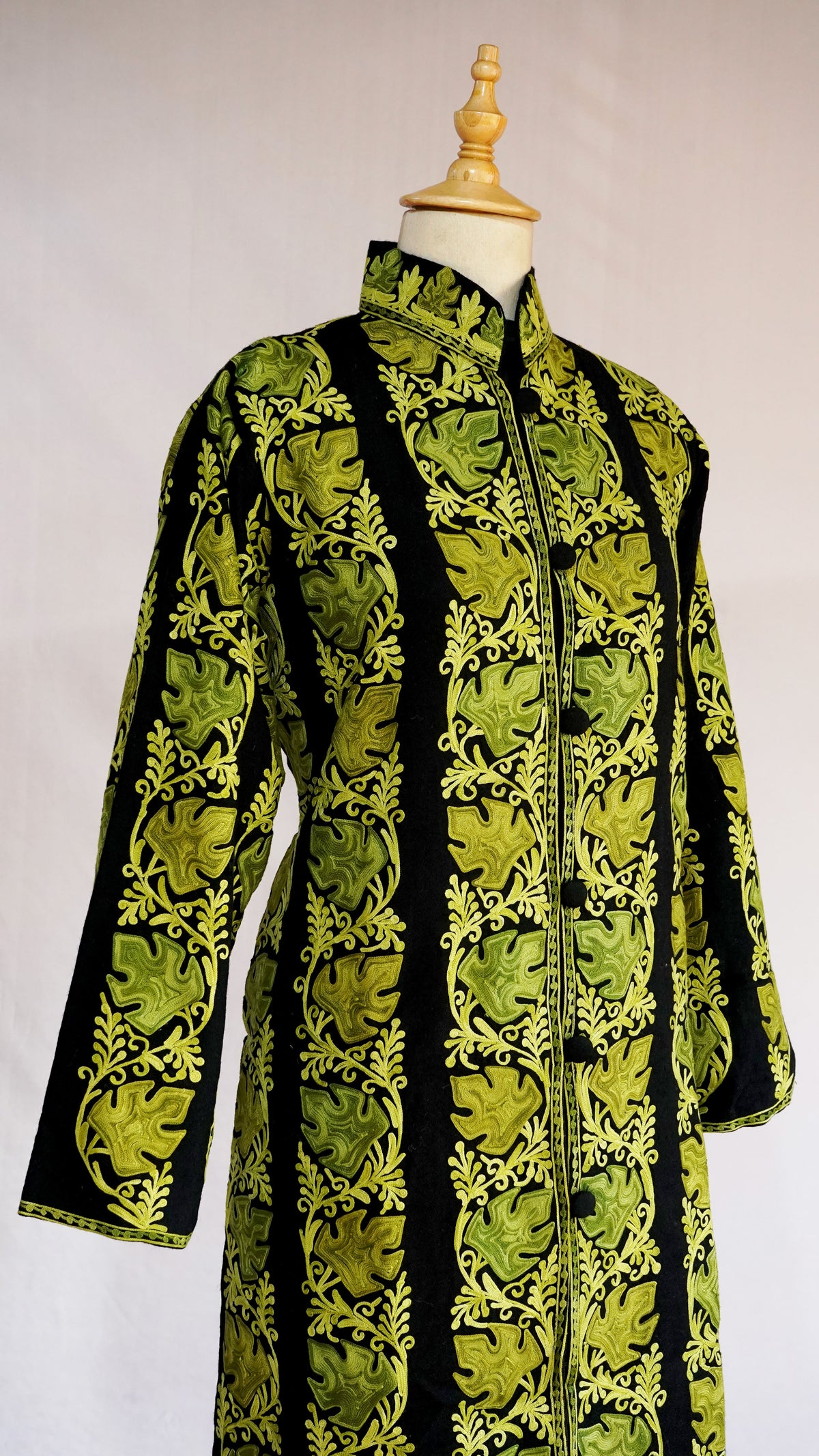 Three-quarter view of a black jacket with chartreuse vertical leaf bands, long sleeves and a stand collar.