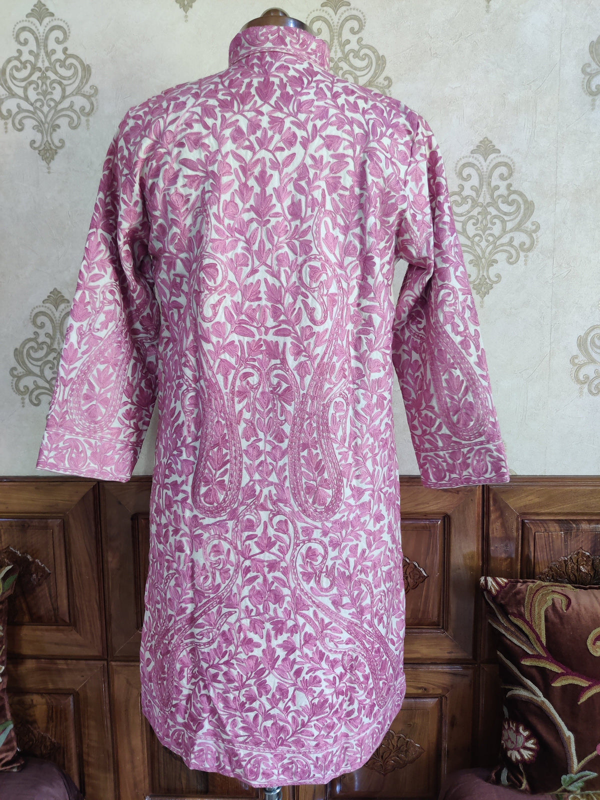 Back of a cream long jacket covered in pink Aari flowers and leafy vines, with an embroidered high collar