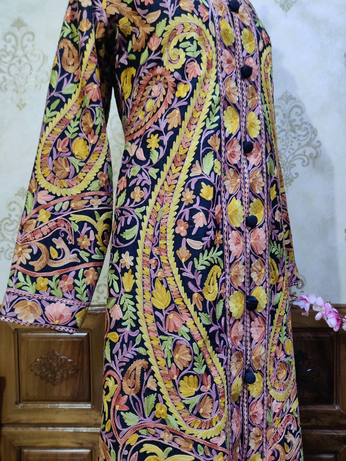 Close-up of the jacket front and sleeve with a long yellow-green Aari paisley, pink stems and small brown and yellow flowers
