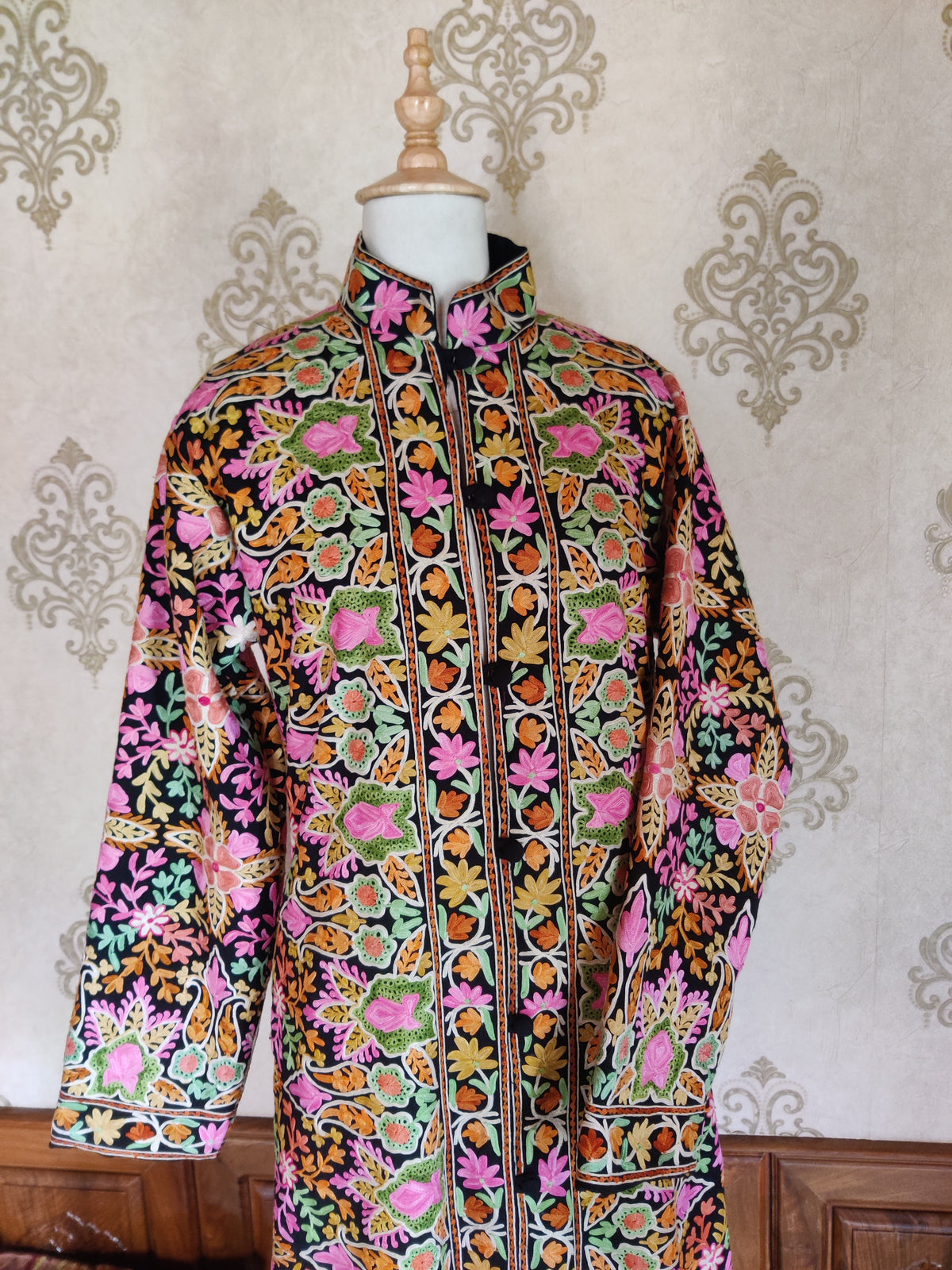 Black Aari jacket front with a stand collar, multicoloured floral panels and one sleeve folded across the waist