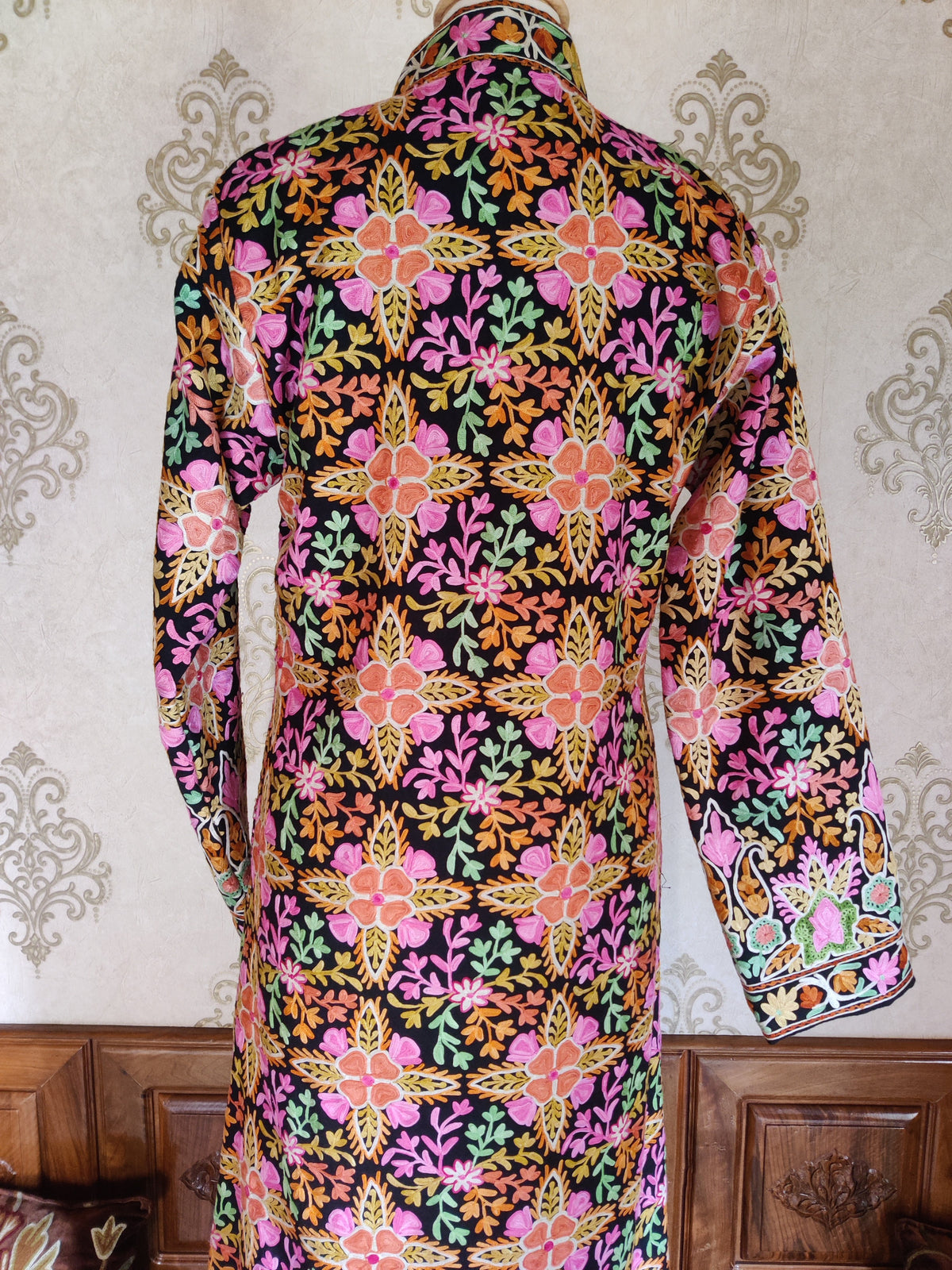 Upper back of a black Aari jacket with rows of pink-orange flowers, yellow pointed leaves and colourful branching sprigs