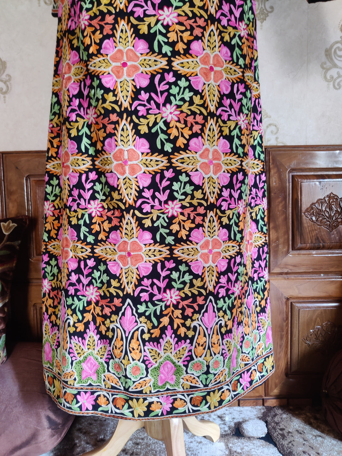 Lower back of a black Aari jacket with repeating pink-orange flowers above a multicoloured floral hem border
