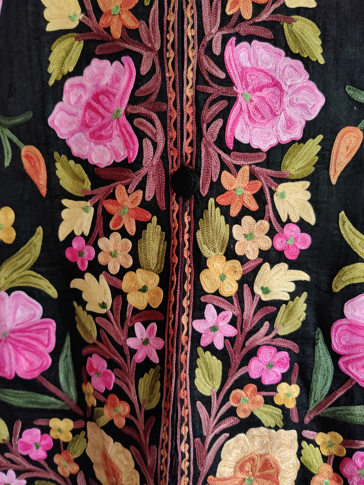 Close-up of black jacket front panels with bright pink Aari flowers, small pastel blossoms and green leaves beside the buttons