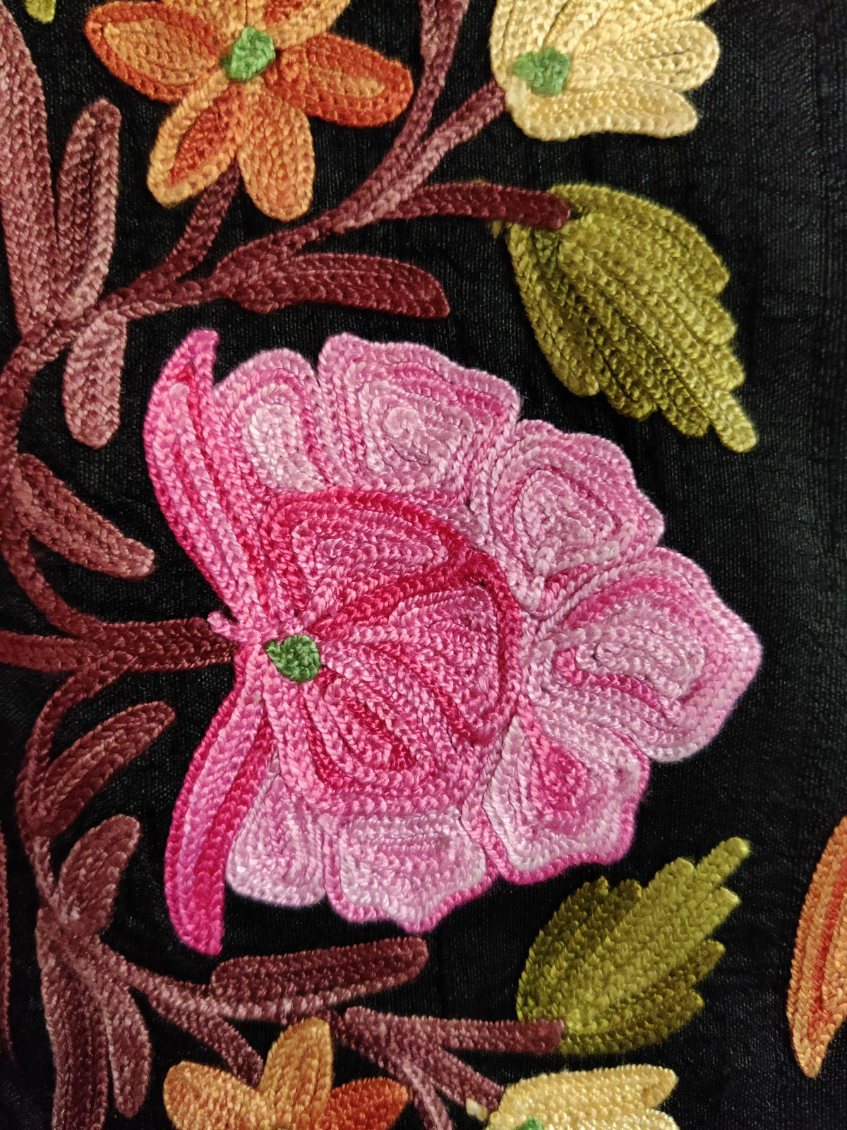 Macro detail of a two-tone pink Aari flower with green leaves and mauve stems on a black jacket