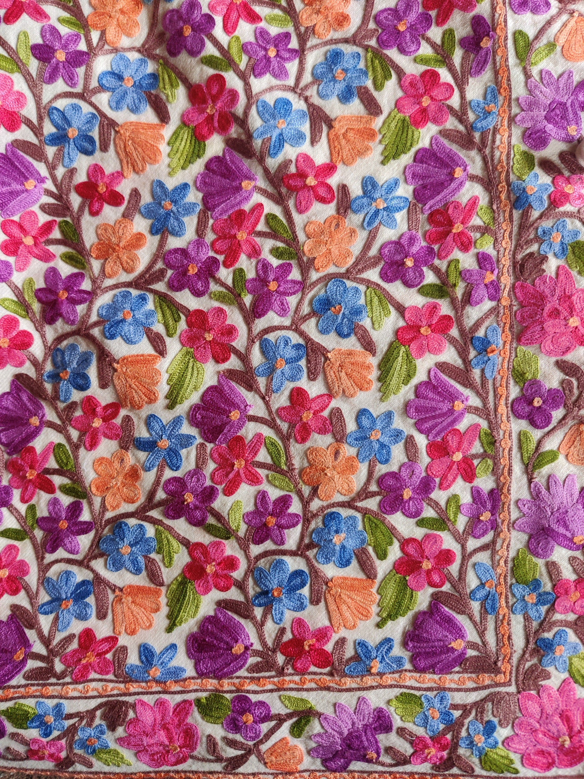 Close-up of blue, purple, pink and orange Aari flowers along the white jacket's lower front and hem border