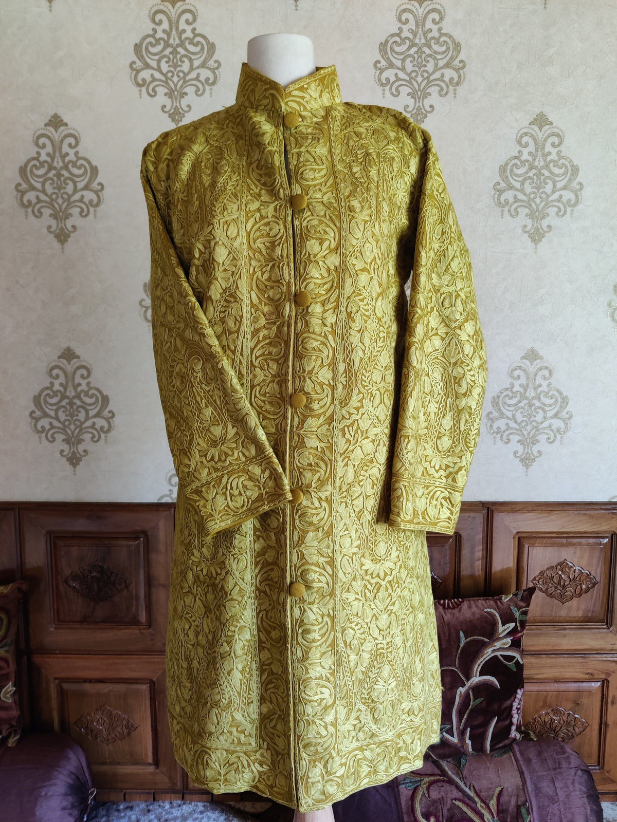 Front of the mustard-yellow Aari jacket on a mannequin with one sleeve folded inward, showing tonal floral paisleys.