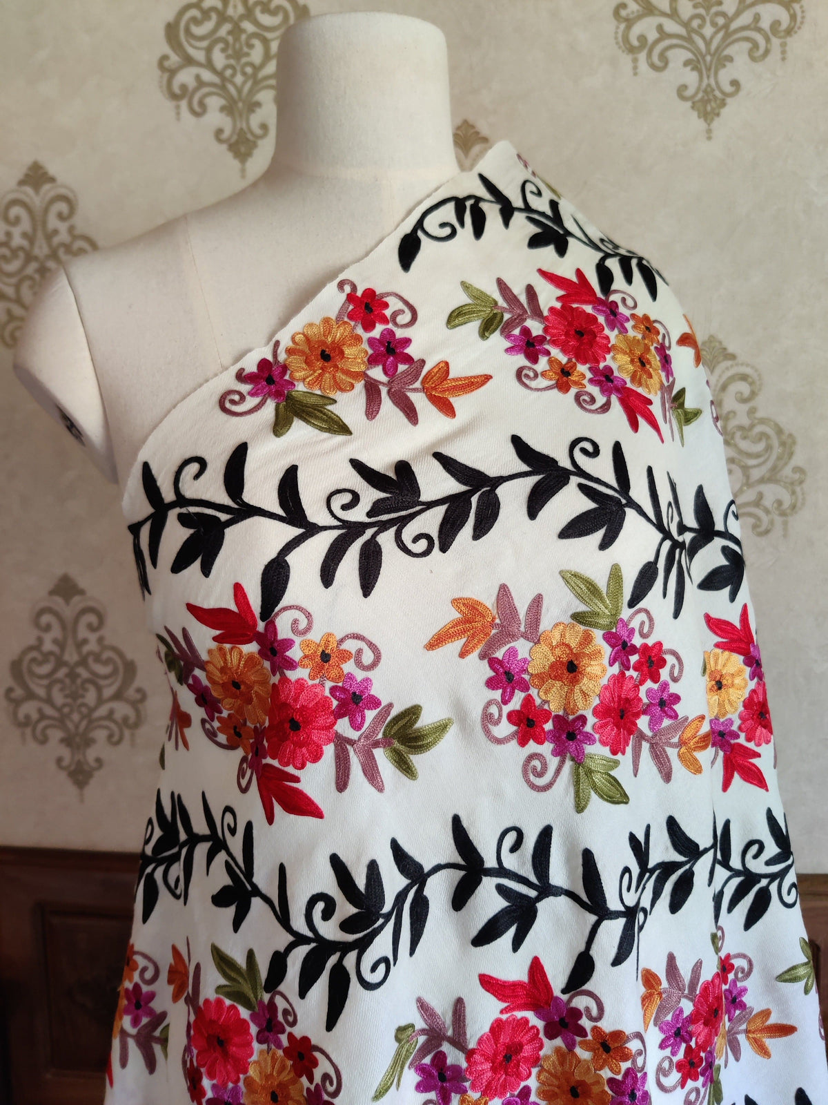 Upper view of a white merino wool stole on a mannequin, with red, pink and orange Aari flower clusters and black leafy vines.