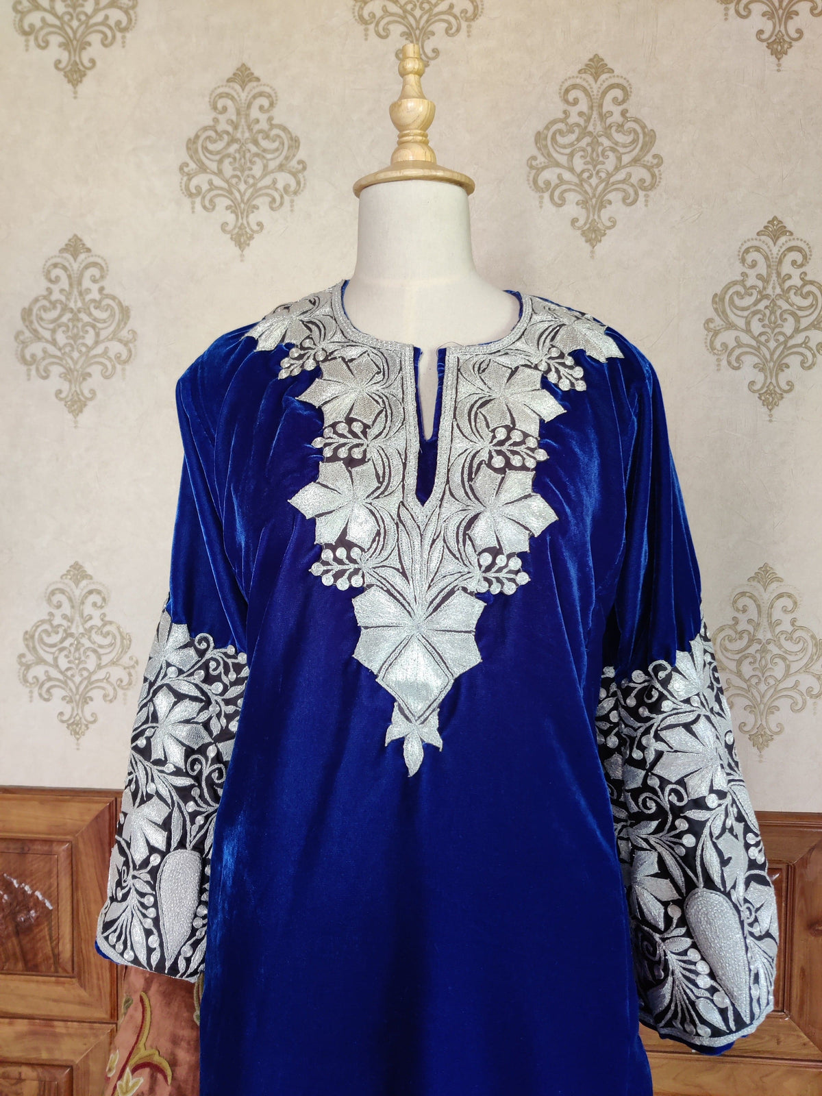 Upper front detail of the blue velvet pheran with a pointed silver-toned floral neckline and broad embroidered cuffs.