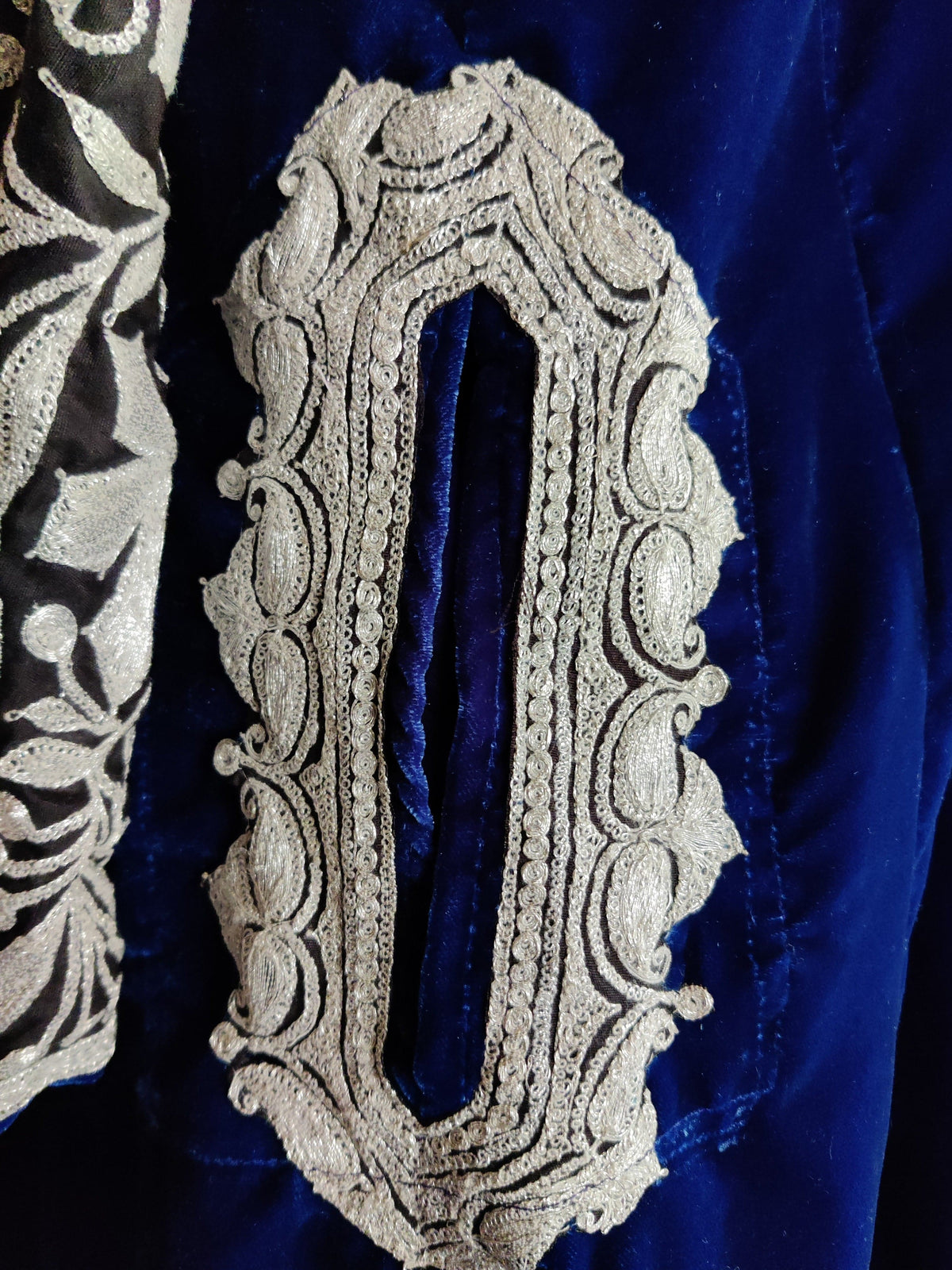Close-up of a pocket opening framed in silver-toned scrolling embroidery on royal-blue velvet.