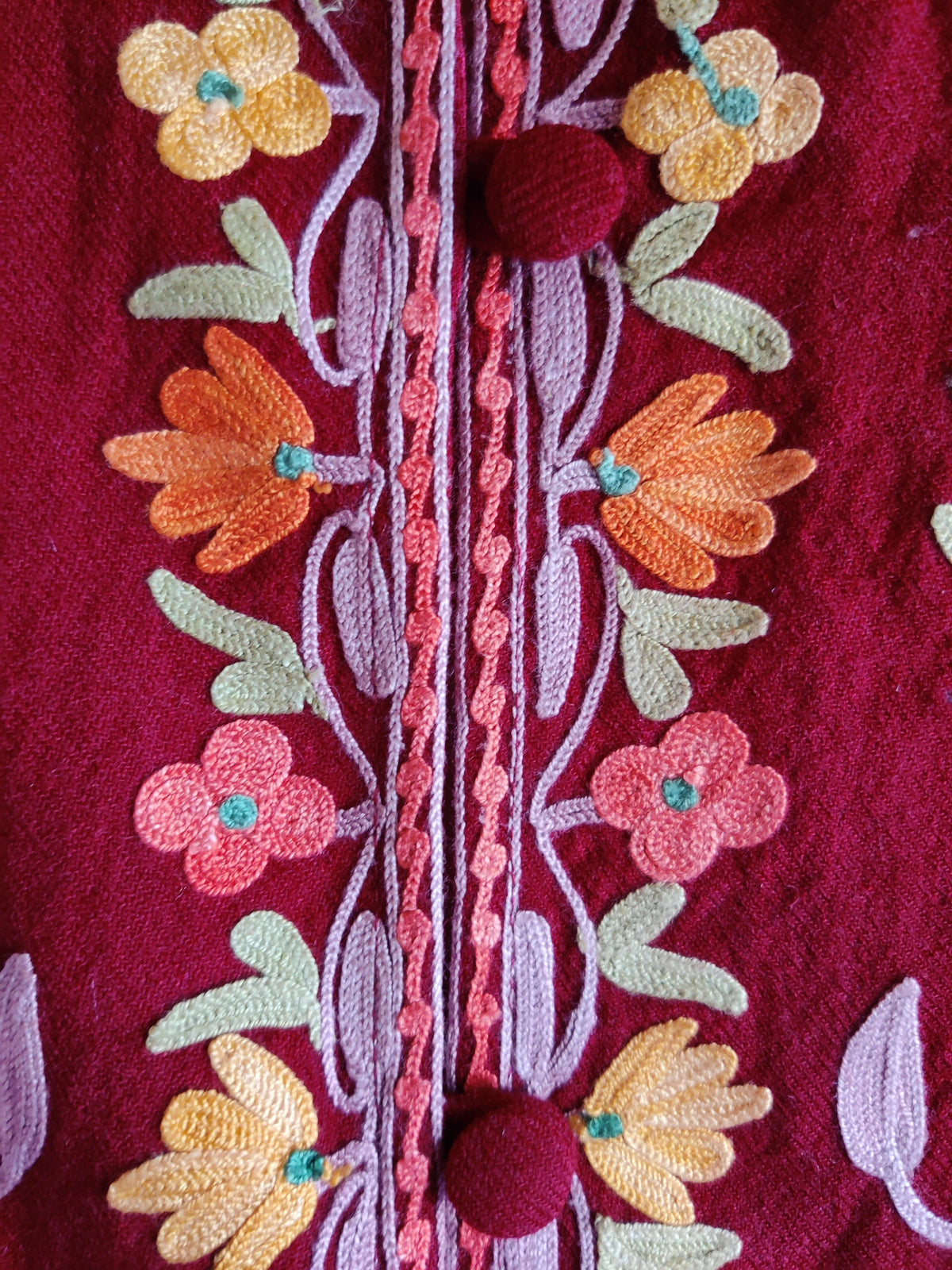 Close-up of maroon covered buttons framed by small pink, peach and yellow Aari flowers and lilac stems