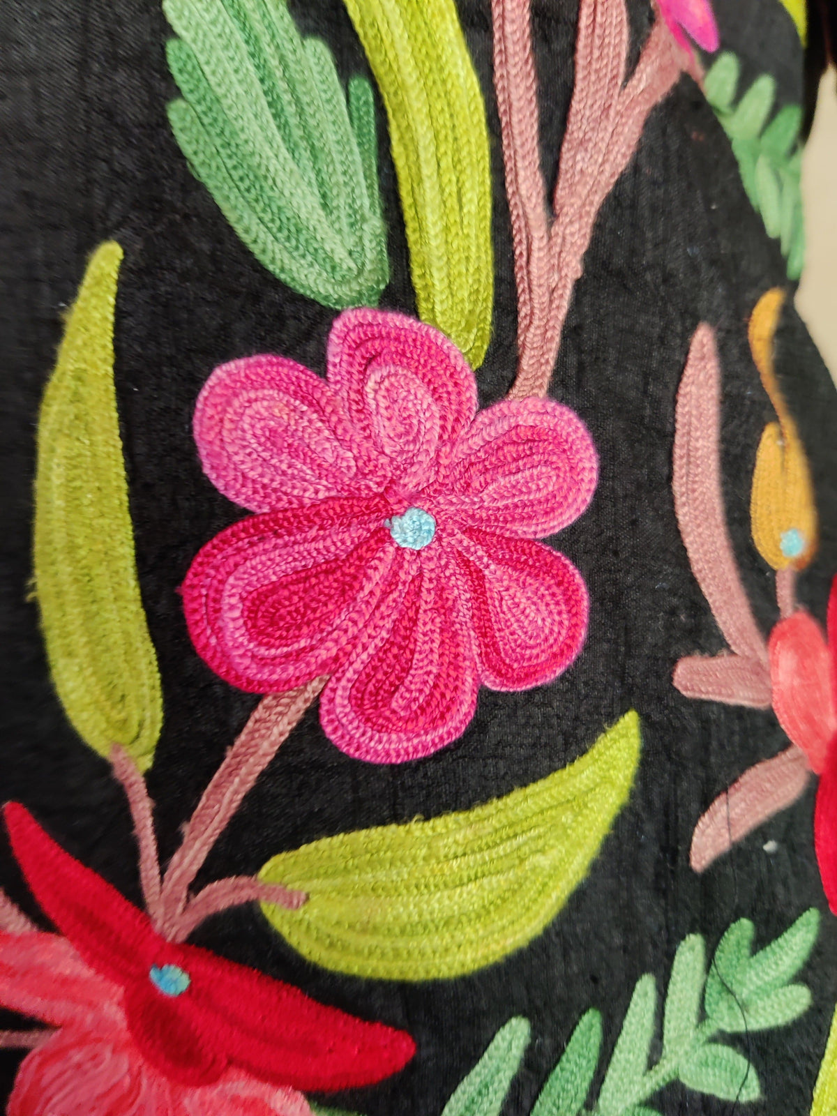 Macro detail of a pink Aari flower, lime-green leaves and pale pink stems on the black jacket