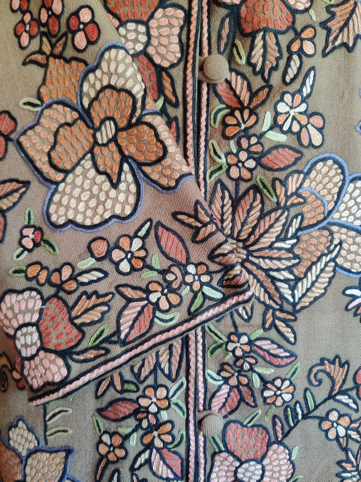 Close-up of the beige wool jacket’s crossed cuff and front buttons, with pastel floral Hand Aari embroidery