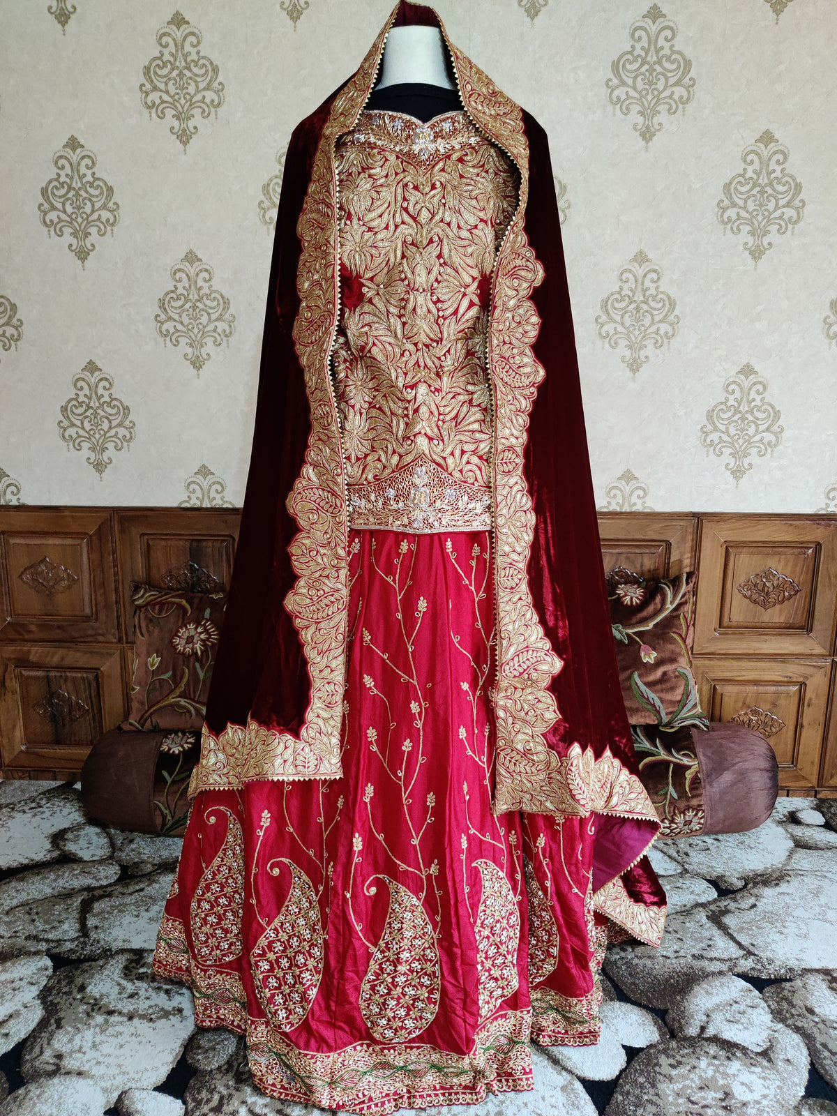 Front view of a red silk lehenga ensemble with dense golden Tilla embroidery, large skirt paisleys and a maroon dupatta over the mannequin’s head