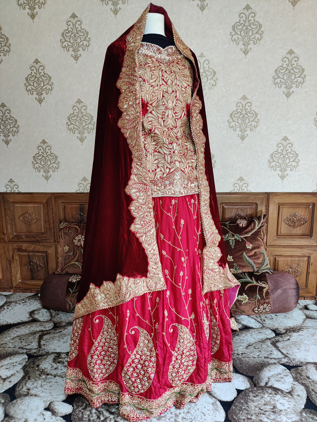 Angled full view of the red lehenga on a mannequin, showing gold skirt paisleys and a maroon velvet dupatta with scalloped borders