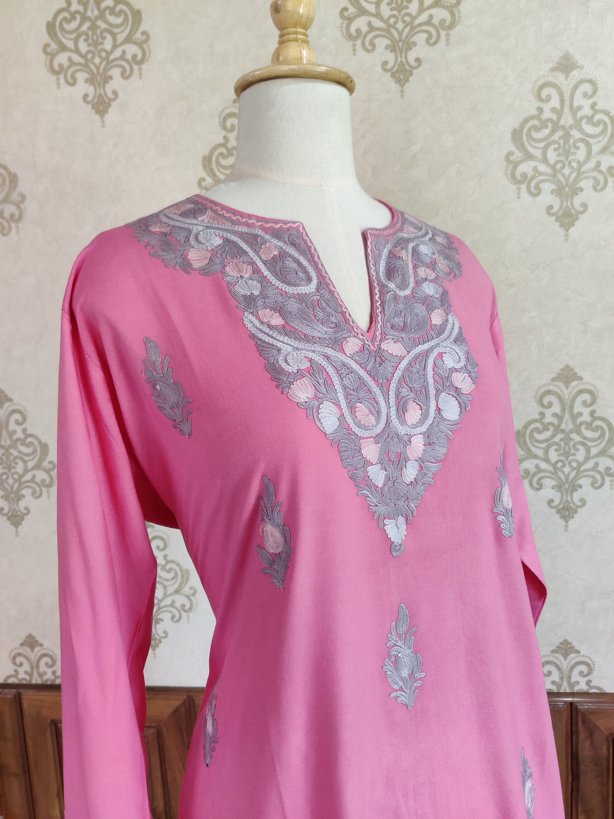 Angled view of a pink kurti with a grey and cream Aari embroidered neckline and scattered floral motifs