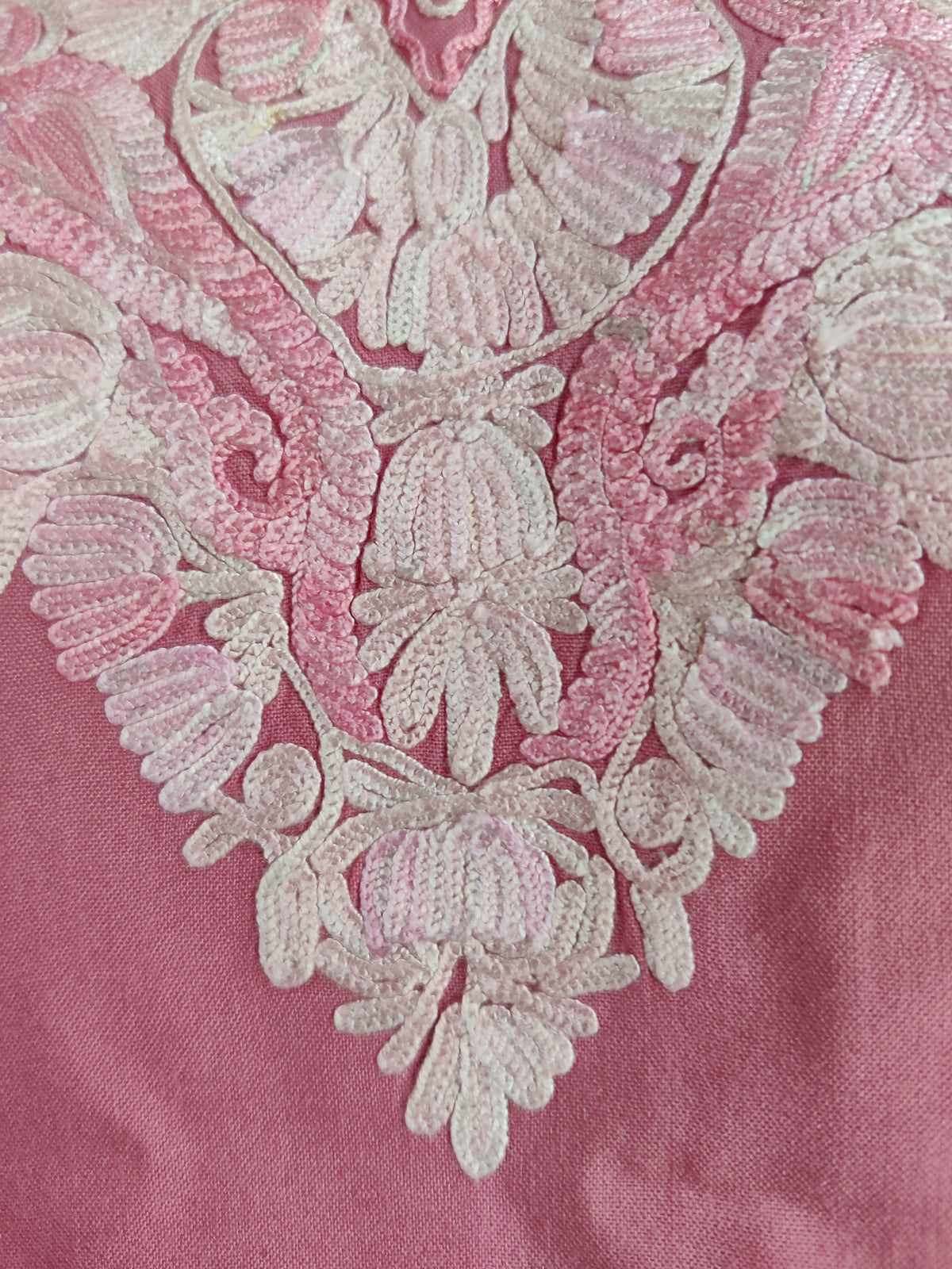 Macro detail of white floral embroidery with pale-pink shading at the pointed base of the kurti neckline.
