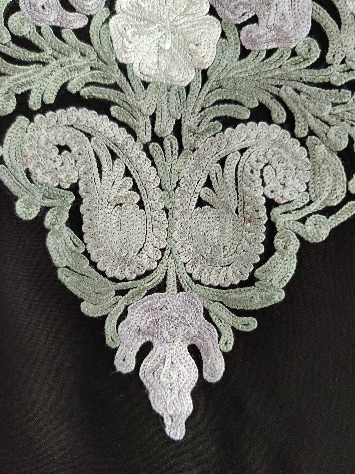 Close-up of paired pale mint Aari paisleys and a lilac flower at the point of a black kurti neckline panel