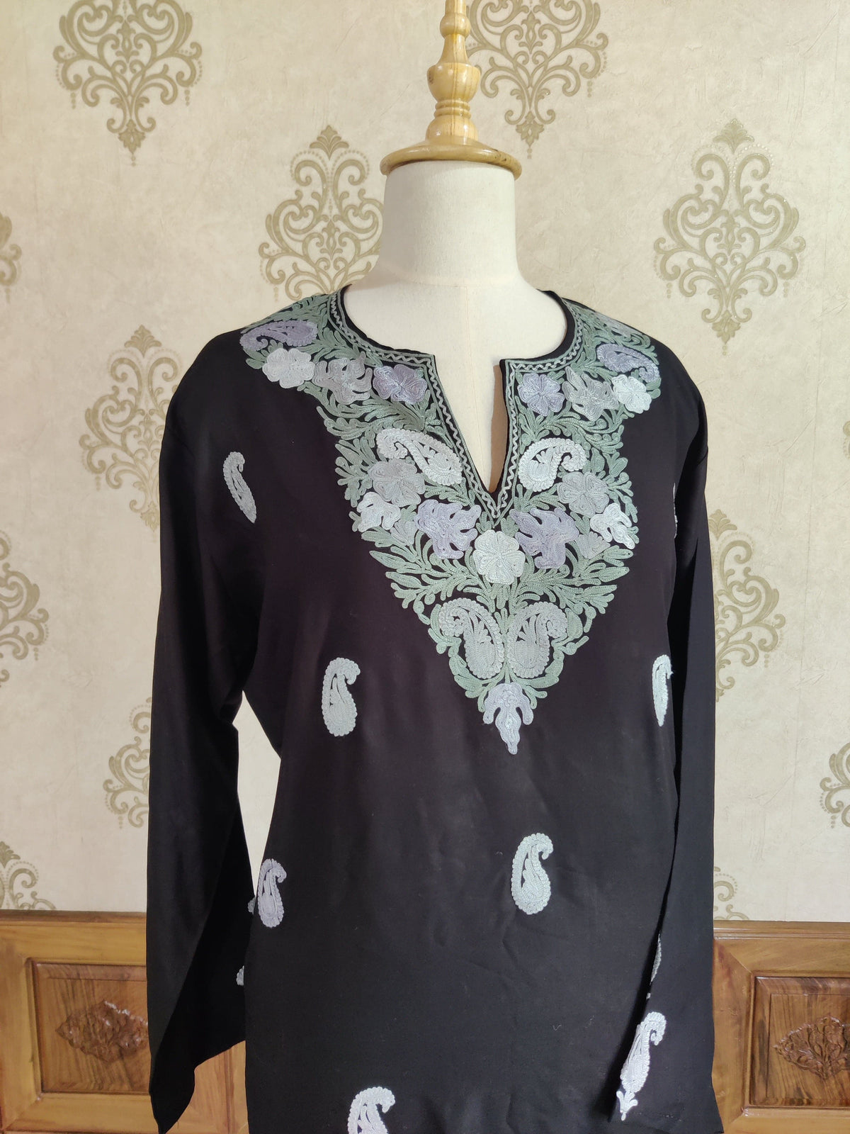 Angled front of a black kurti with mint and lilac Aari neckline embroidery and scattered pale paisley motifs