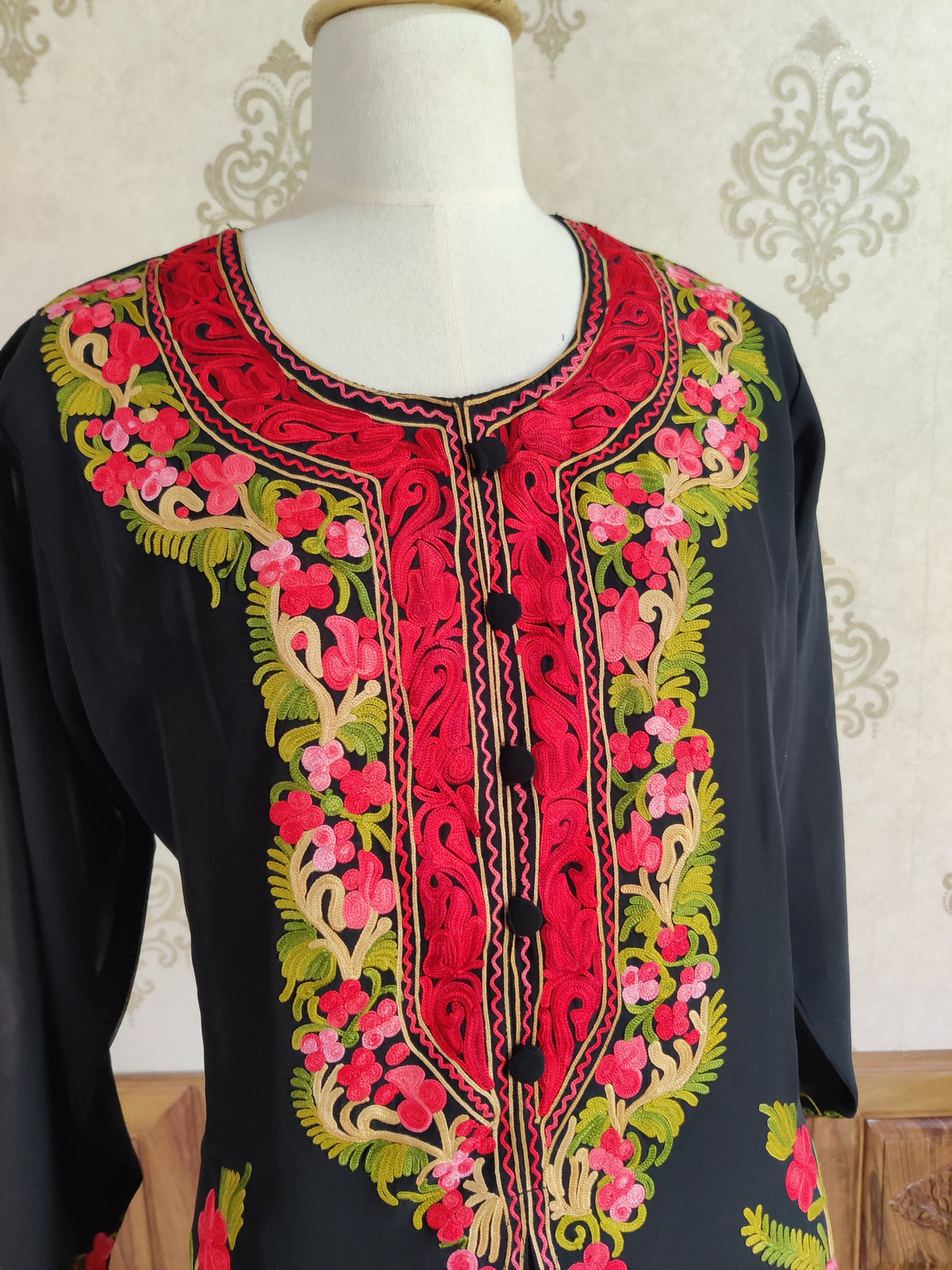 Close-up of the black kaftan neckline with red scrolling embroidery inside pink and green Aari floral borders