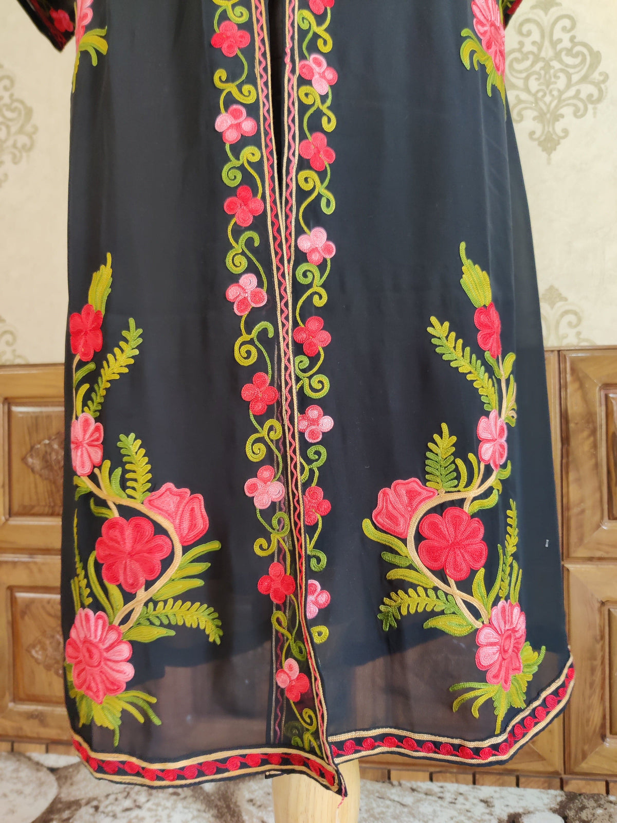 Lower front of a black kaftan with pink Aari floral sprigs, a slim centre vine border and an embroidered hem