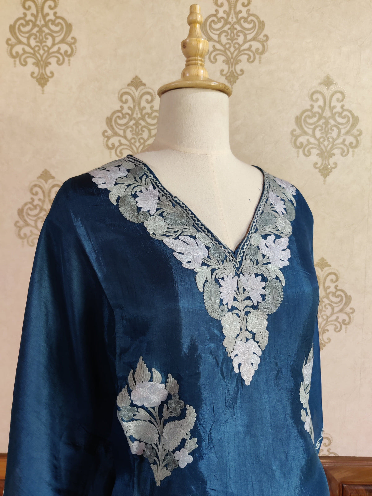 Angled neckline view of the blue kaftan, showing white and silver-grey flowers and leaves around the V-neck.