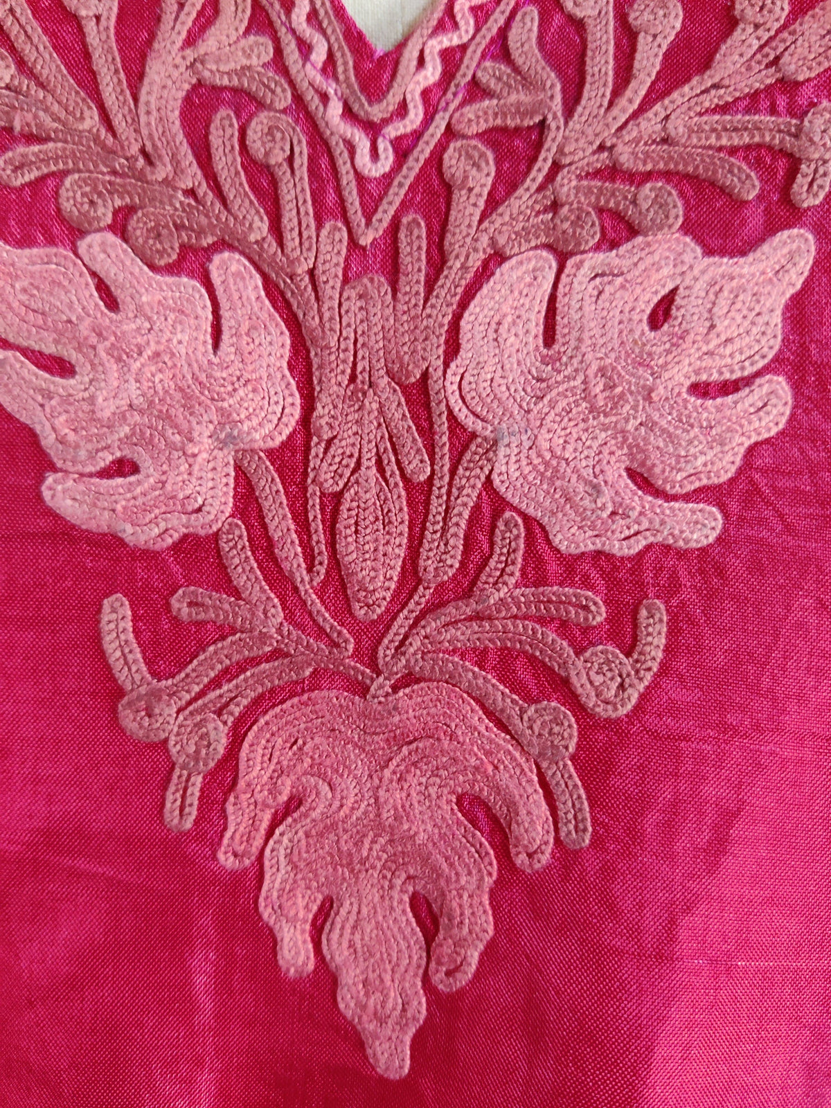 Close-up of pale pink lobed leaves and curling stems in the fuchsia kaftan’s Aari neckline embroidery
