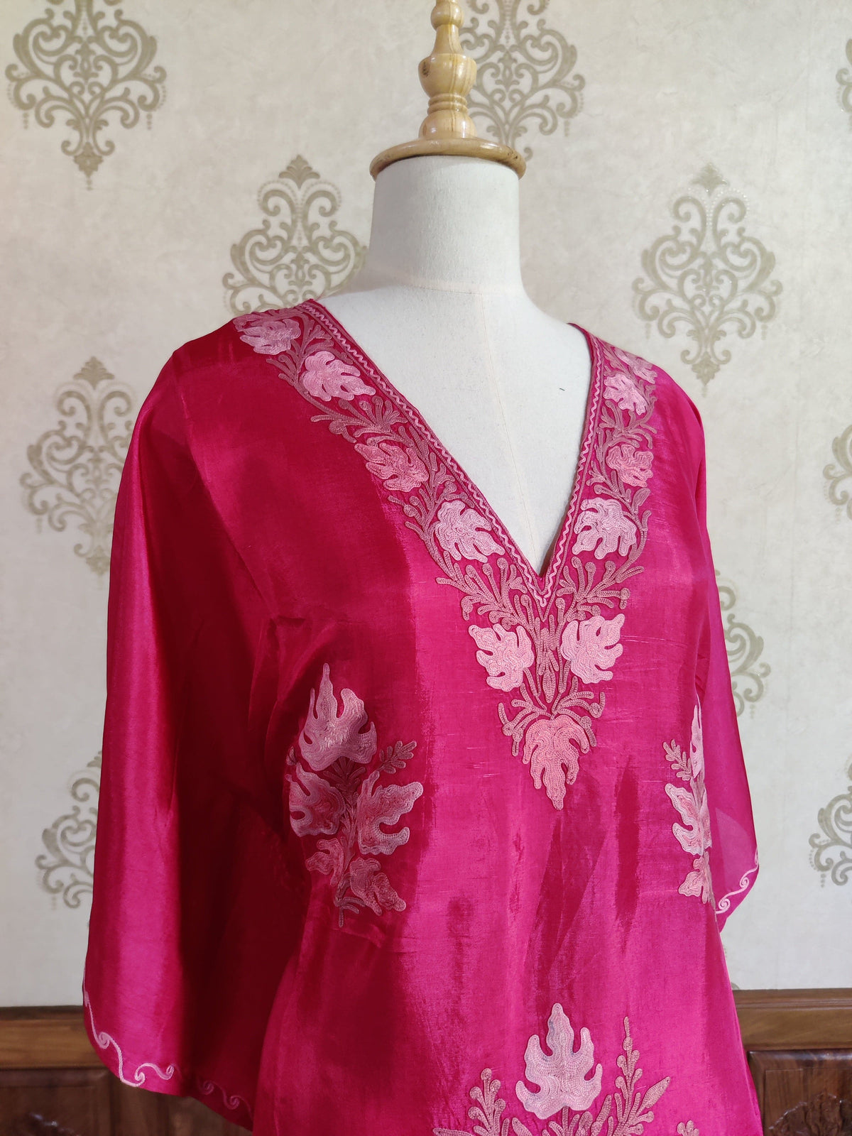 Angled upper view of the fuchsia kaftan on a mannequin, showing loose sleeves and pale pink embroidered neckline and side motifs