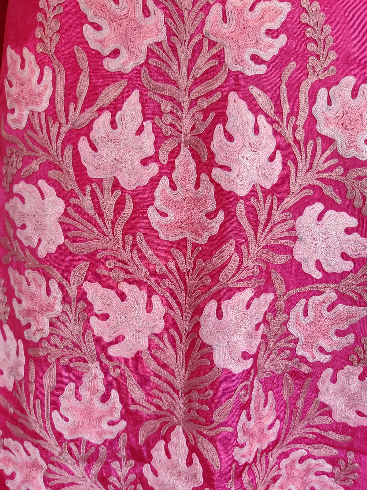 Detailed view of the large pale pink Aari leaf-and-stem pattern across the fuchsia kaftan’s lower front