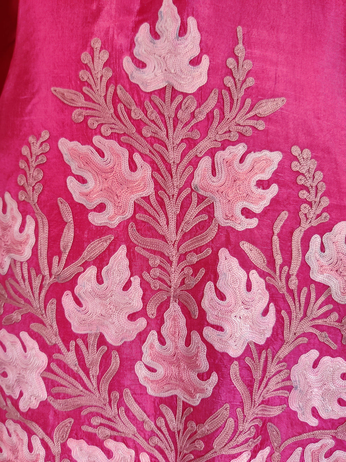Close-up of the fuchsia kaftan’s symmetrical pale pink embroidered leaves branching from a central stem