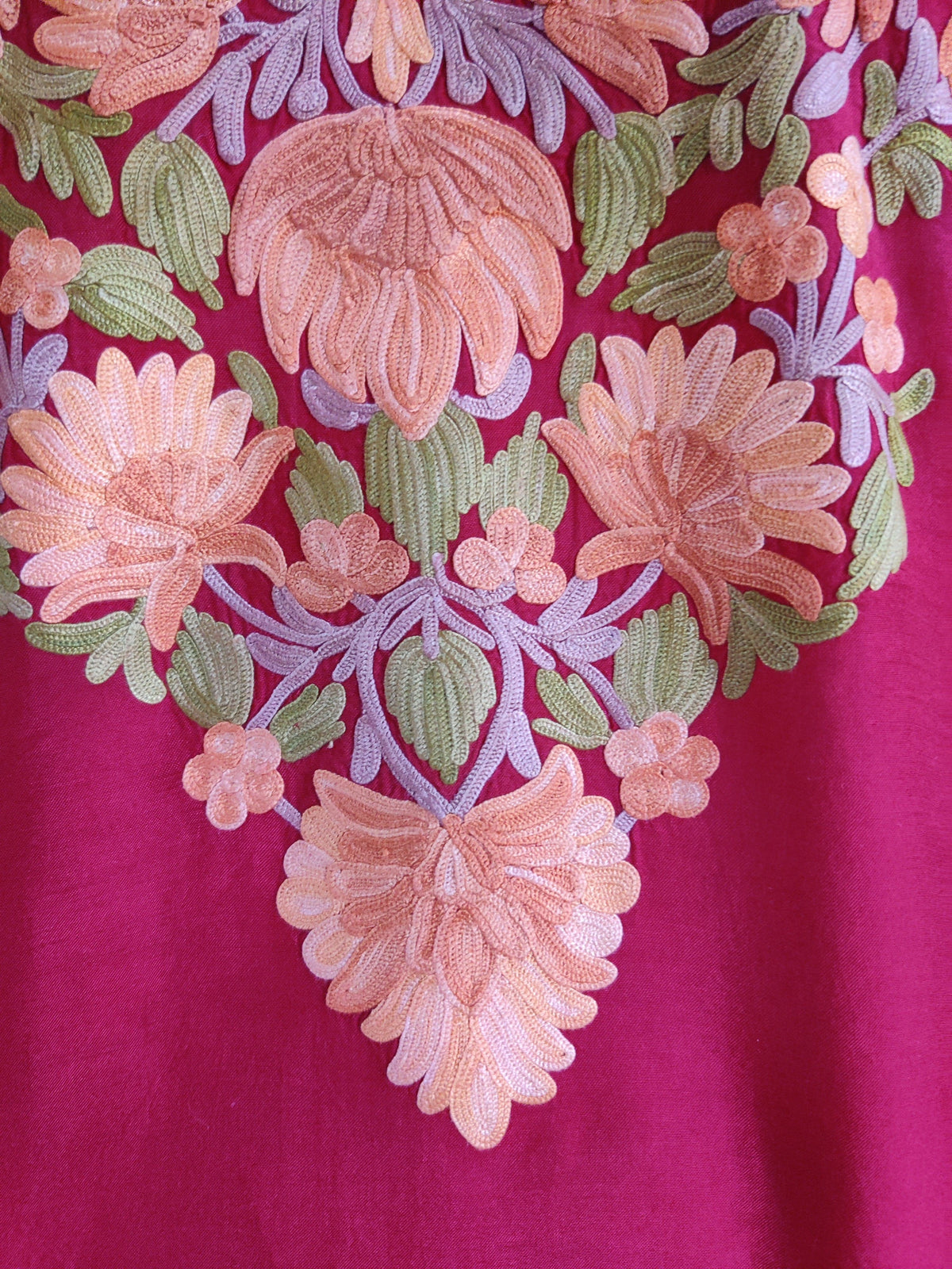 Close-up of peach and pink embroidered flowers with green leaves and lilac stems on fuchsia fabric