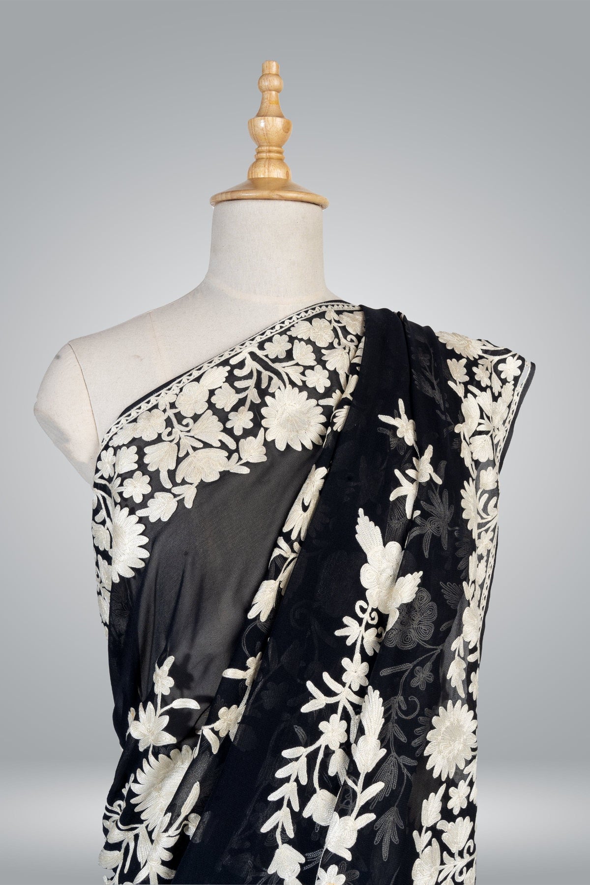 Upper draped view of the black crepe saree on a mannequin, with cream Aari flowers and leafy vines across the shoulder.