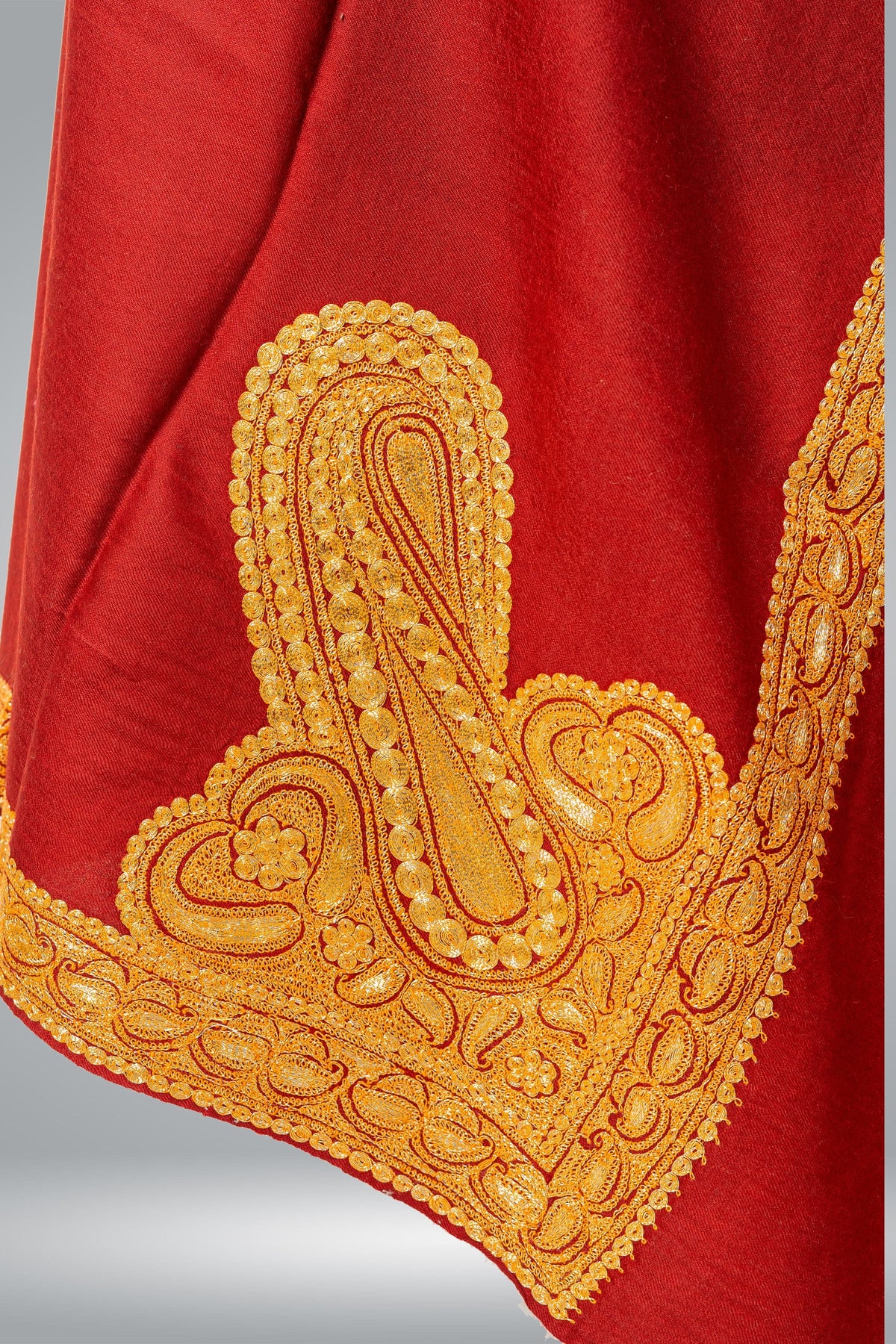 Folded corner of the red Merino wool shawl, with a large golden paisley Tilla motif and embroidered borders