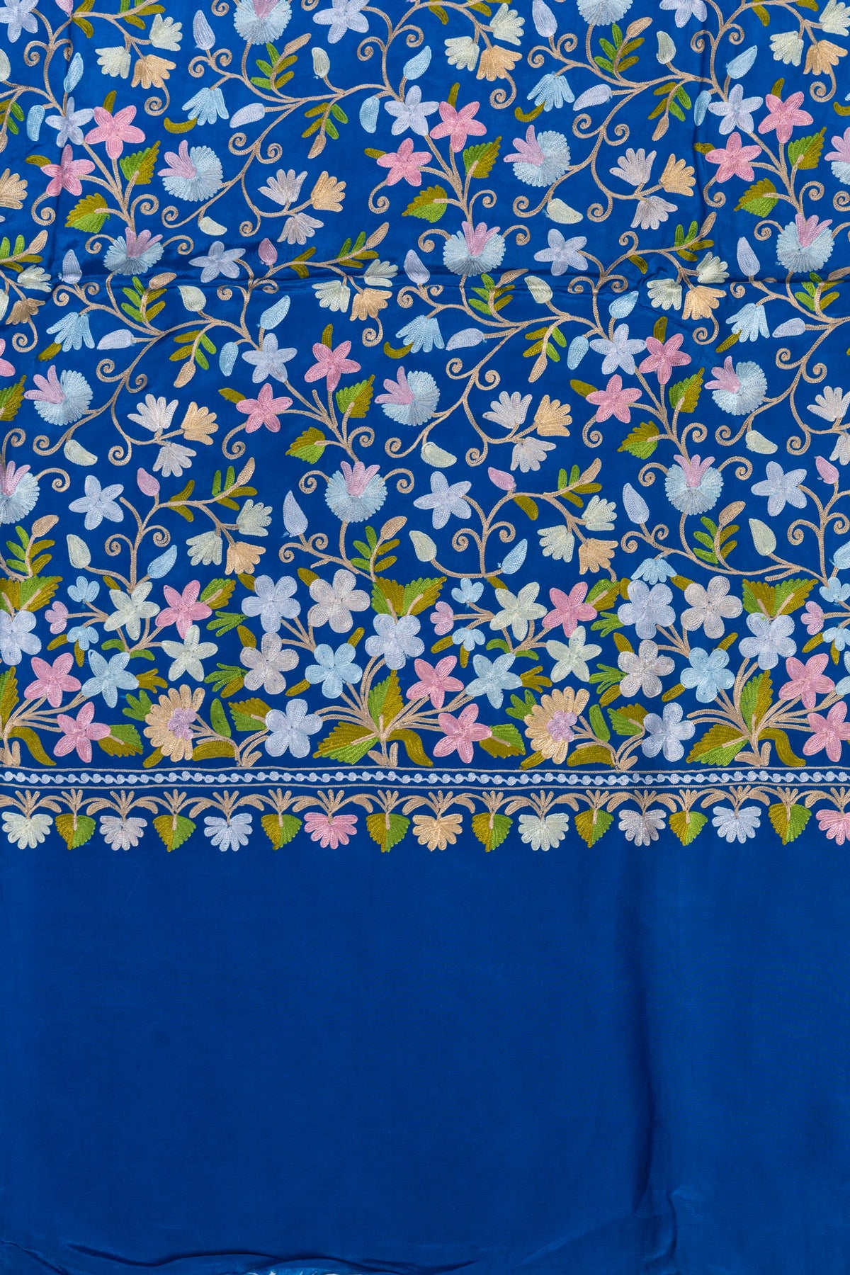 Royal blue sari pallu detail with dense pastel Aari flowers, green leaves and a small floral edging above plain blue fabric