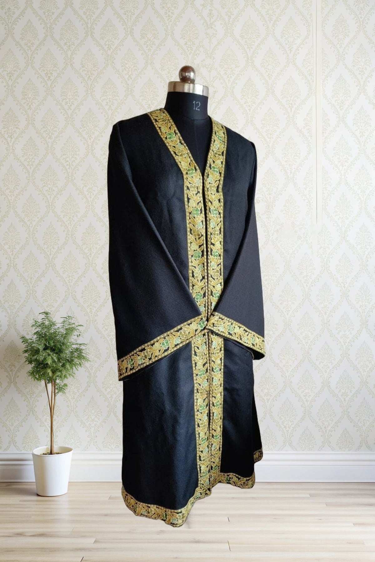 Angled full view of a long black robe with crossed sleeves and gold-and-green floral borders around the opening, cuffs and hem