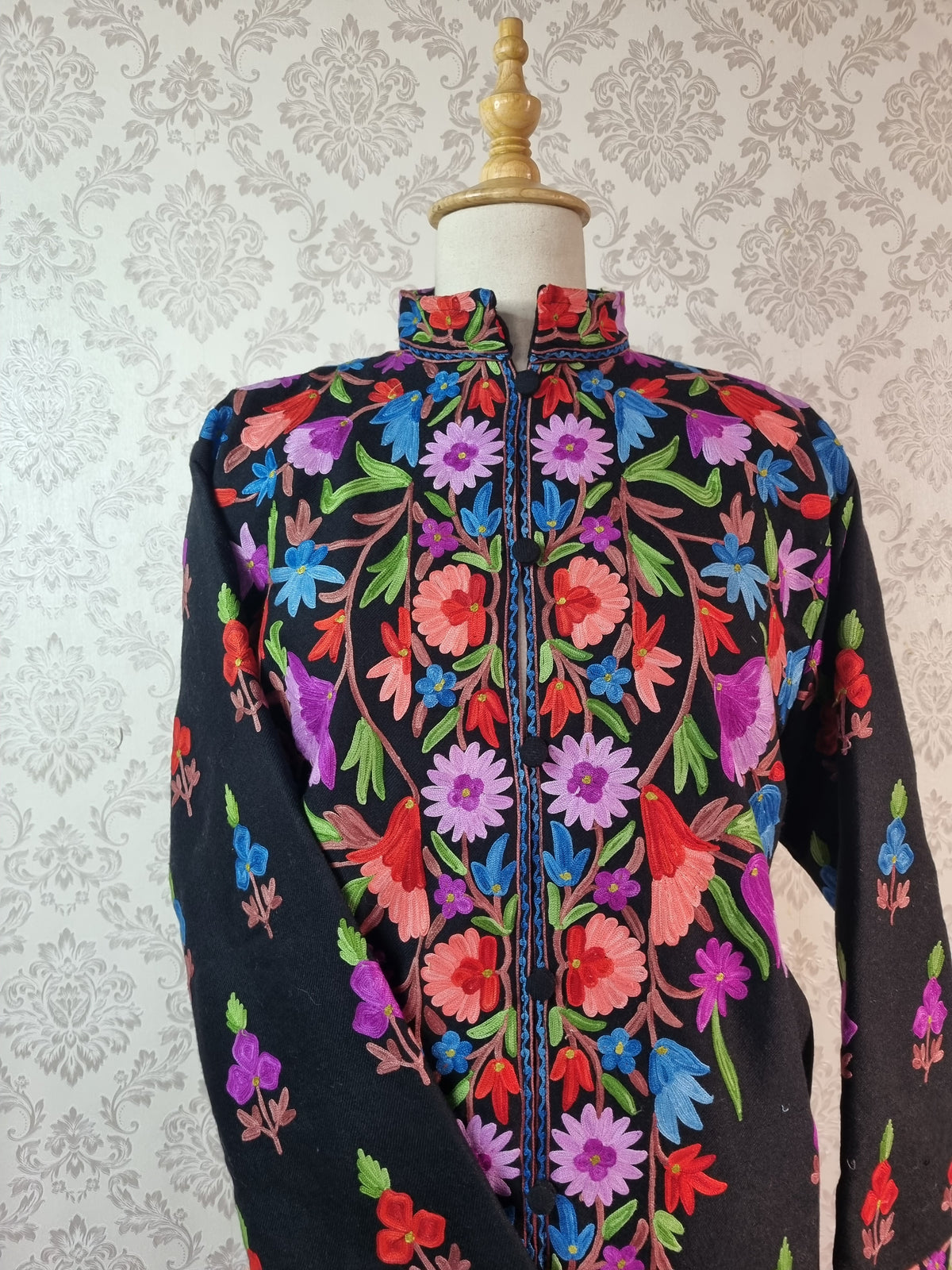 Upper front close-up of the black jacket’s stand collar and dense purple, blue and coral flowers with green leaves.