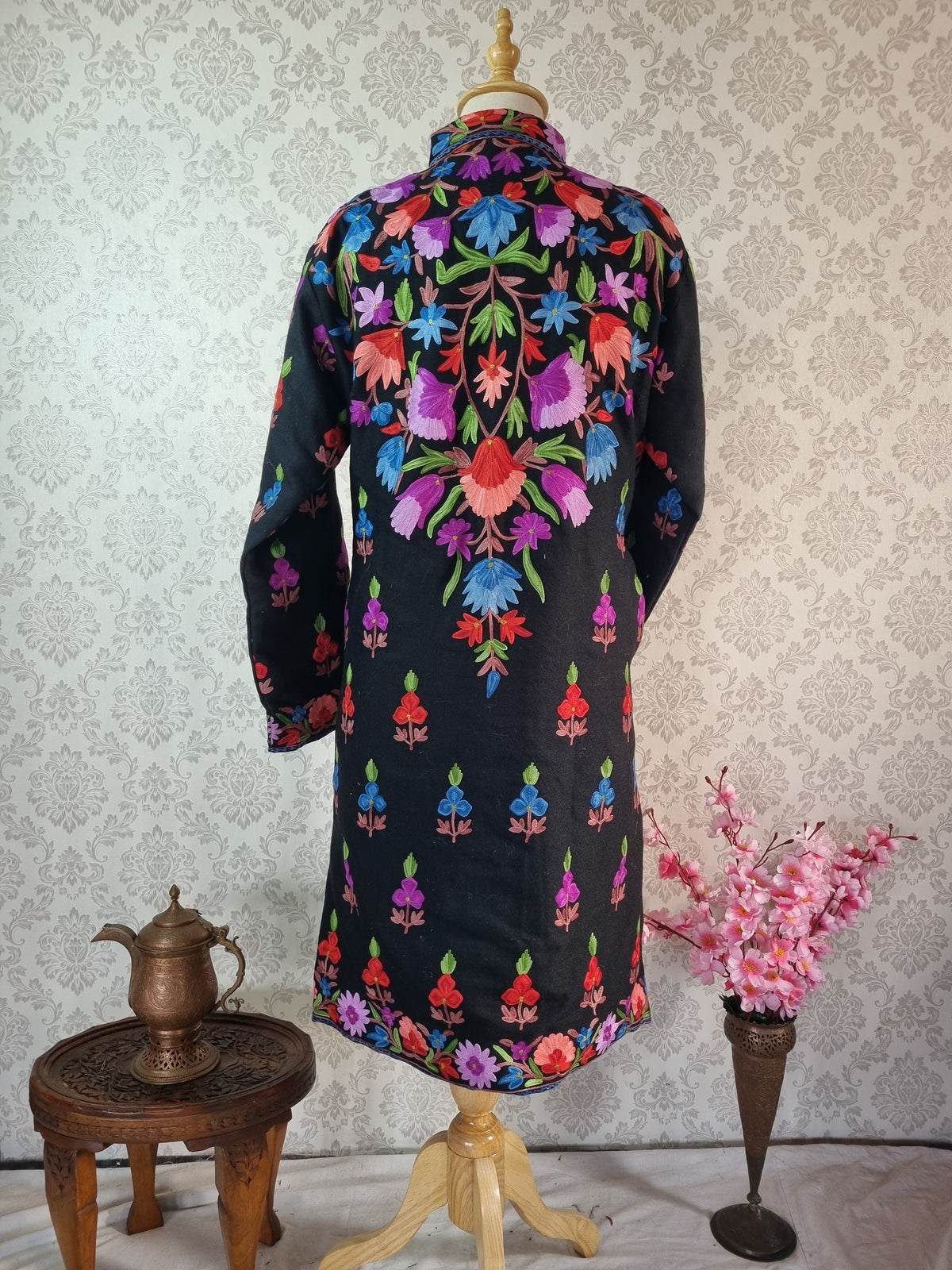 Back of a black jacket with a large pointed floral arrangement across the shoulders and small motifs above the floral hem.