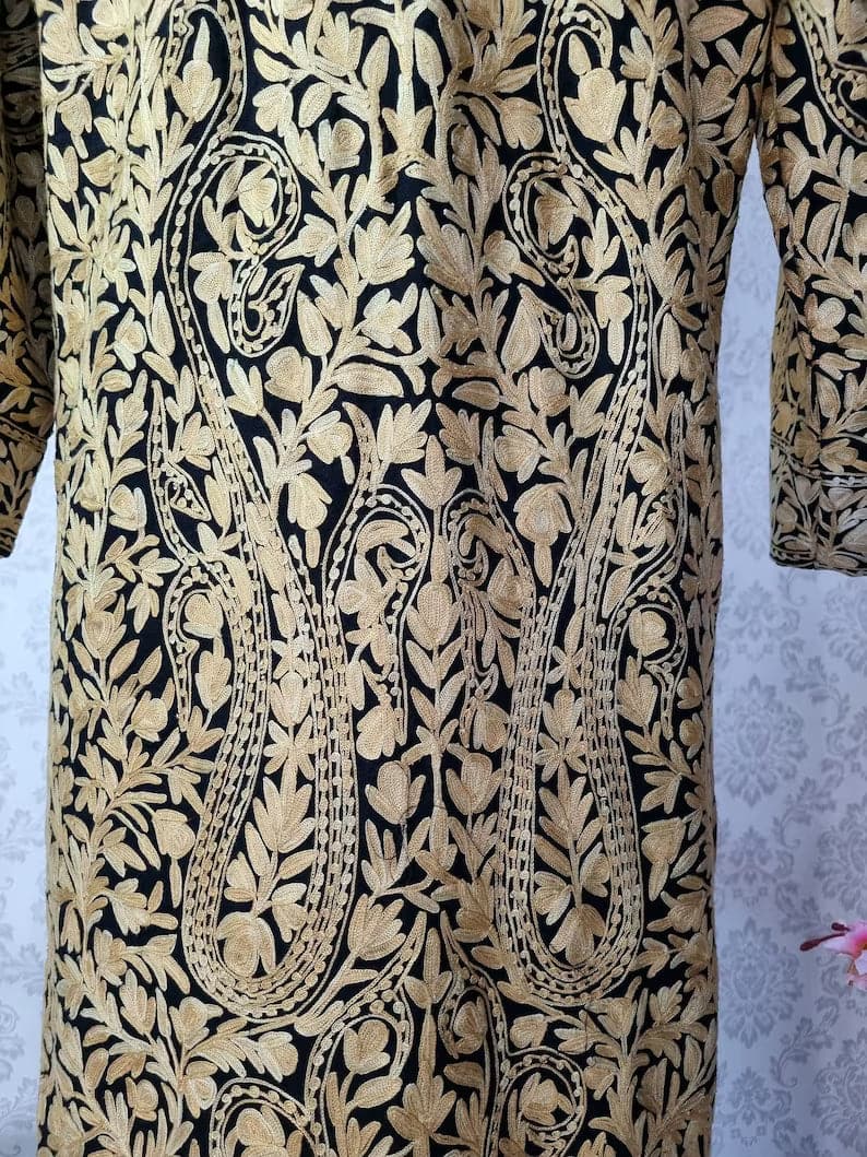 Close-up of large beige Aari paisleys among dense leafy vines on the black jacket's body.