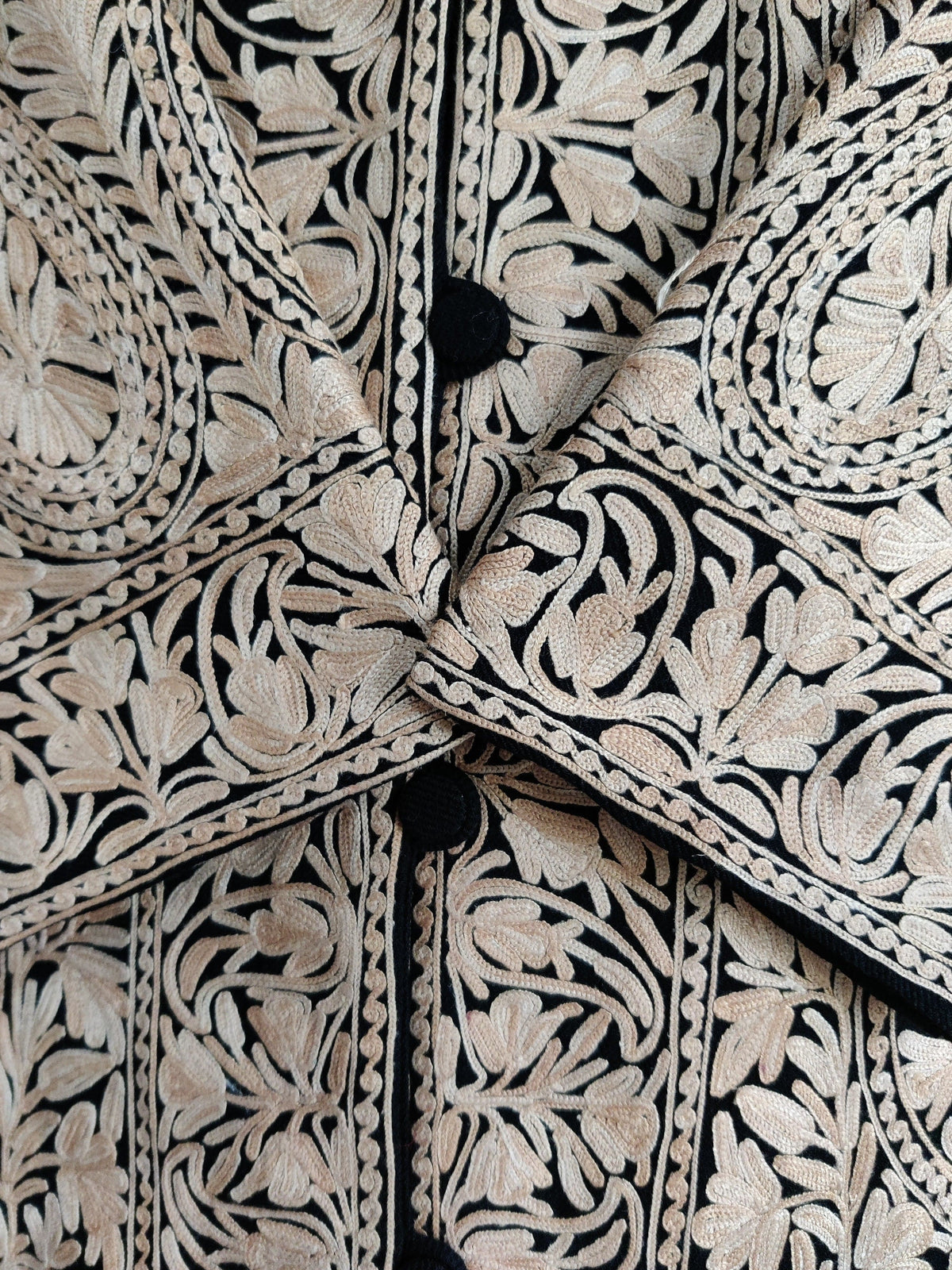Tight detail of almond-toned floral Aari machine embroidery on the Almond Noir jacket’s crossed cuffs and black button placket