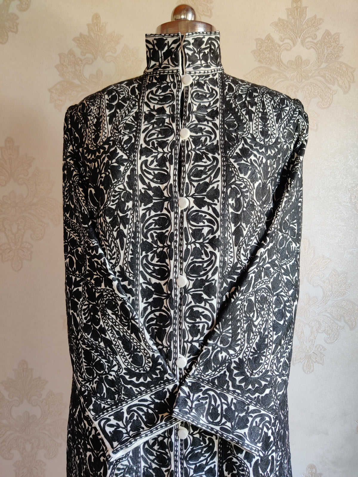 Upper front of the black-and-ivory jacket with round buttons, a stand collar and broad patterned borders beside the fastening.