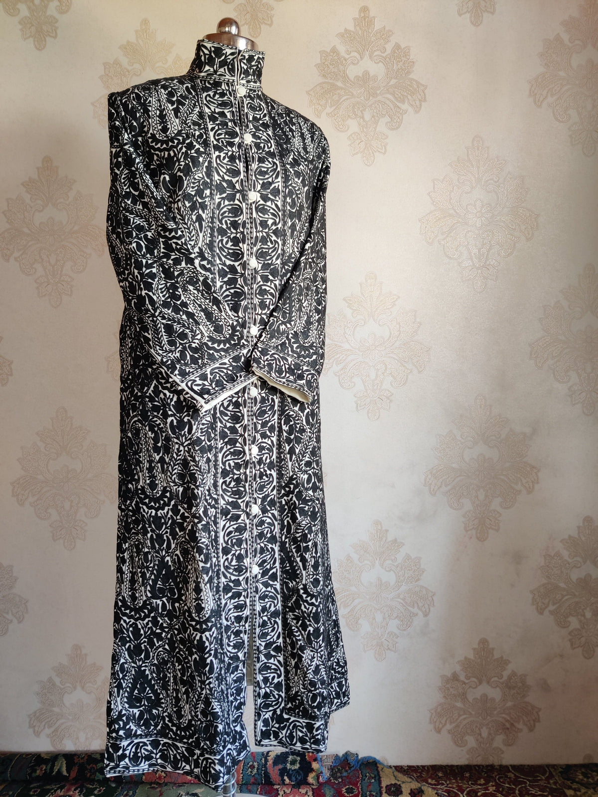 Angled full-length view of a black-and-ivory paisley jacket with crossed sleeves and contrasting floral front borders.
