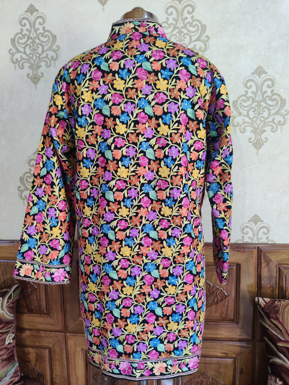Back of the black jacket on a mannequin, densely covered in multicoloured Aari floral vines with matching cuff and hem borders.