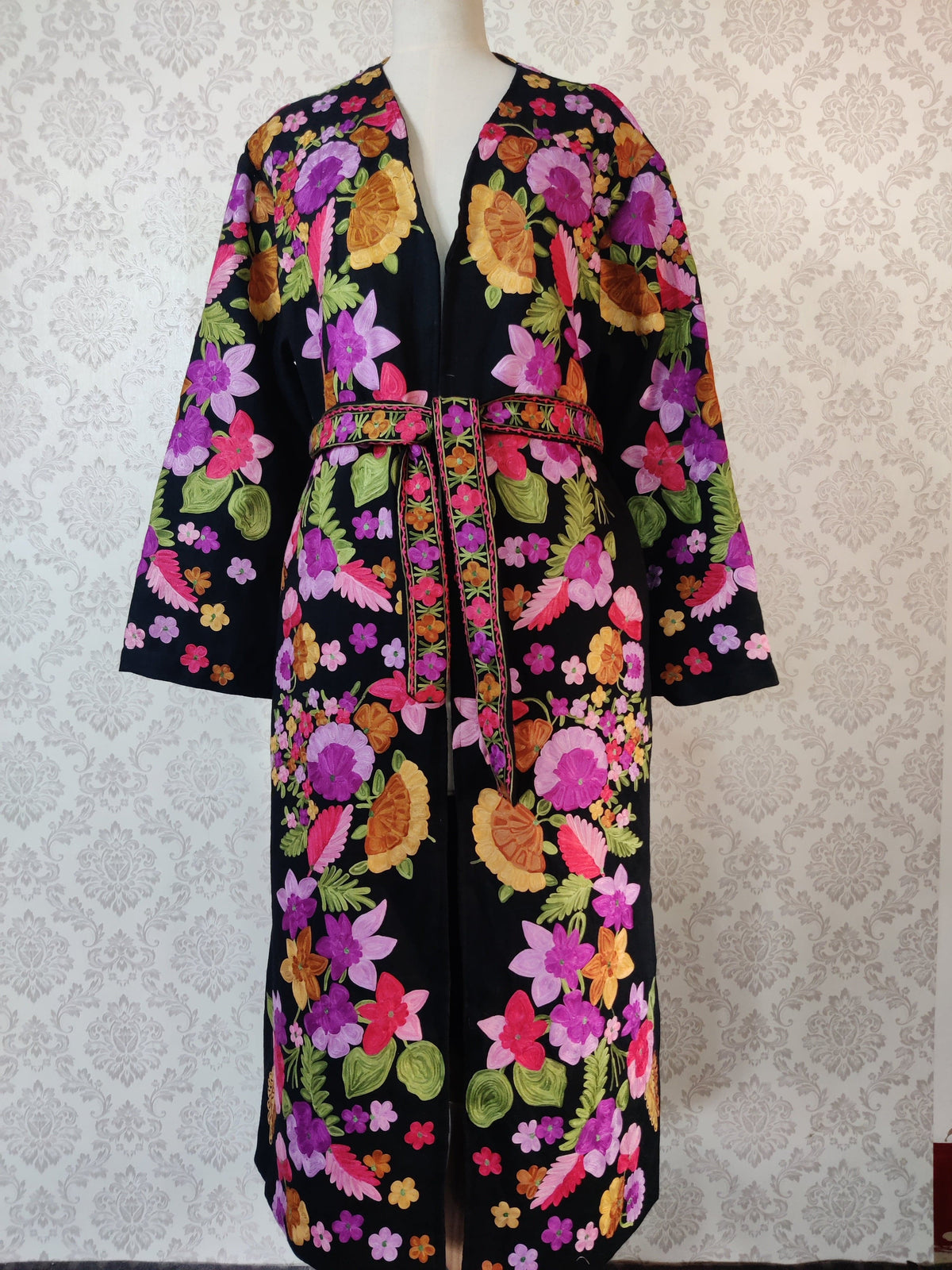 Full front of a belted black robe on a mannequin, with pink, purple and orange embroidered flowers and long hanging floral belt ends.