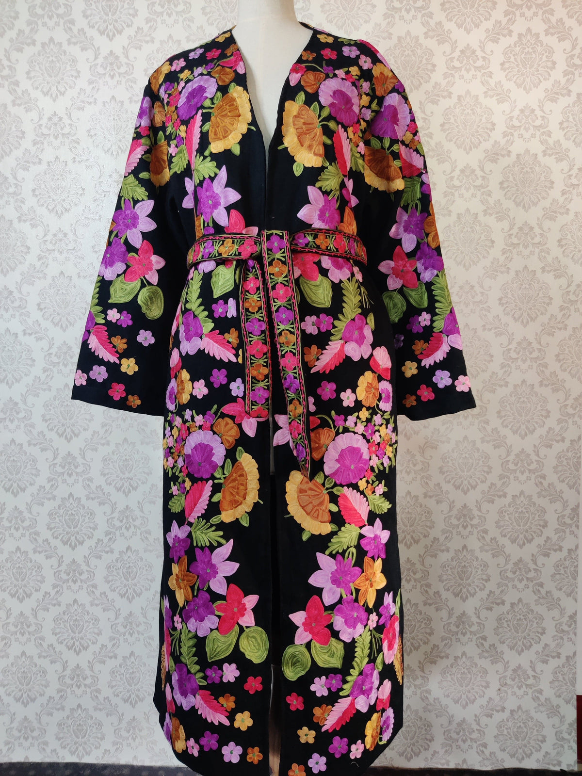 Belted black robe displayed from chest to hem, with bright pink, purple and orange floral embroidery and wide sleeves.