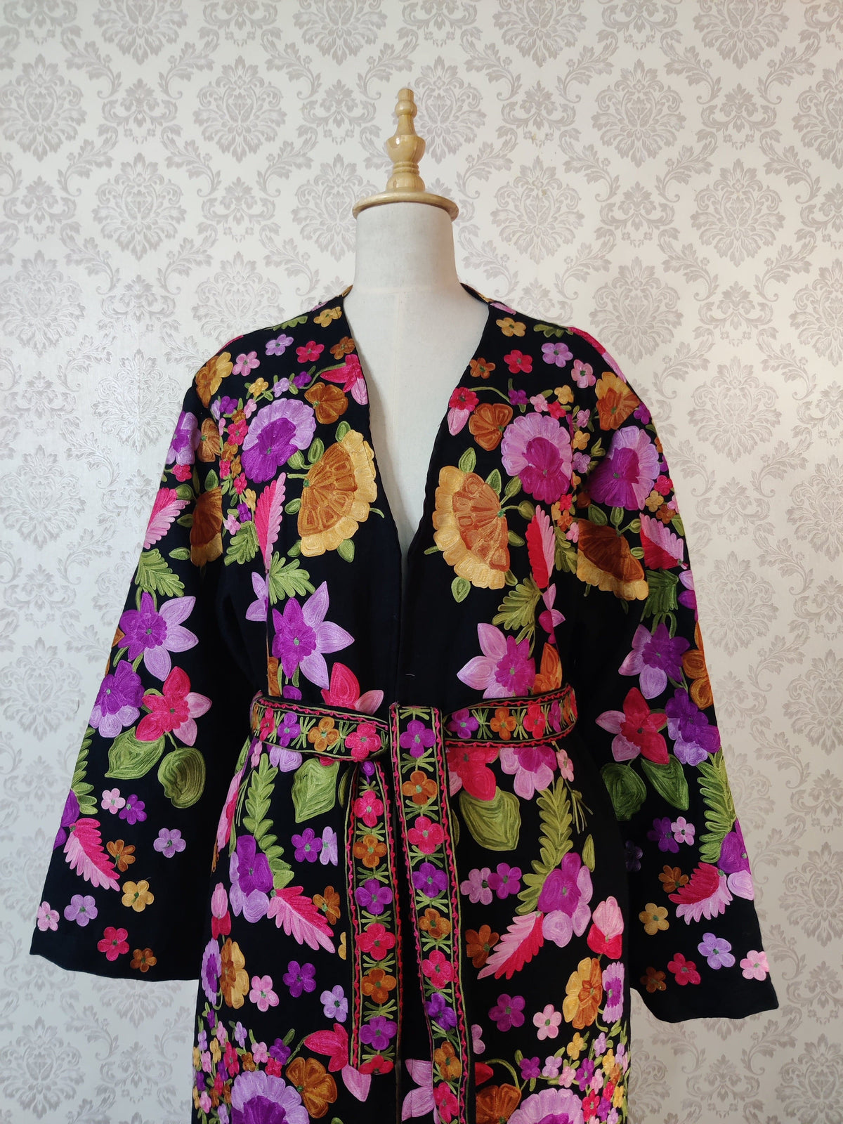 Upper front of a black robe with a floral belt, showing large pink, purple and orange embroidered flowers and wide sleeves.