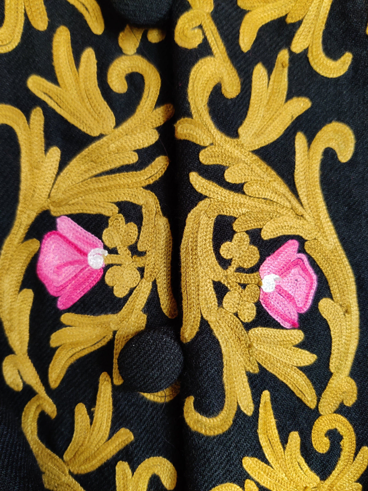 Macro detail of black covered buttons framed by golden Aari leafy vines and small pink flower buds
